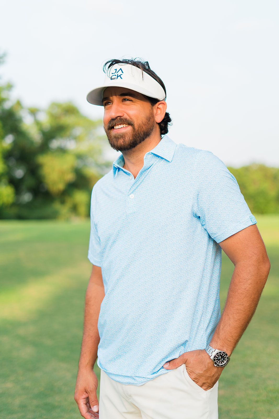 Man wearing a light blue polo shirt and white cap on a grassy field