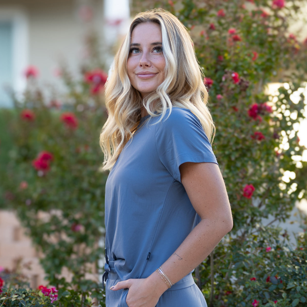 Woman in a blue outfit standing in front of flowering bushes
