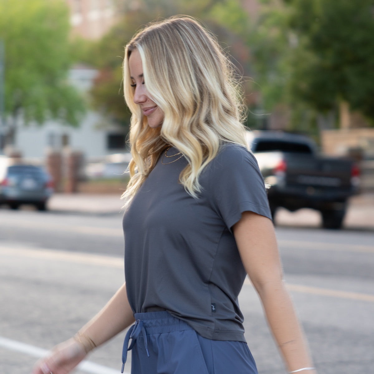 Woman in a gray top and blue pants walking on a street with blurred background