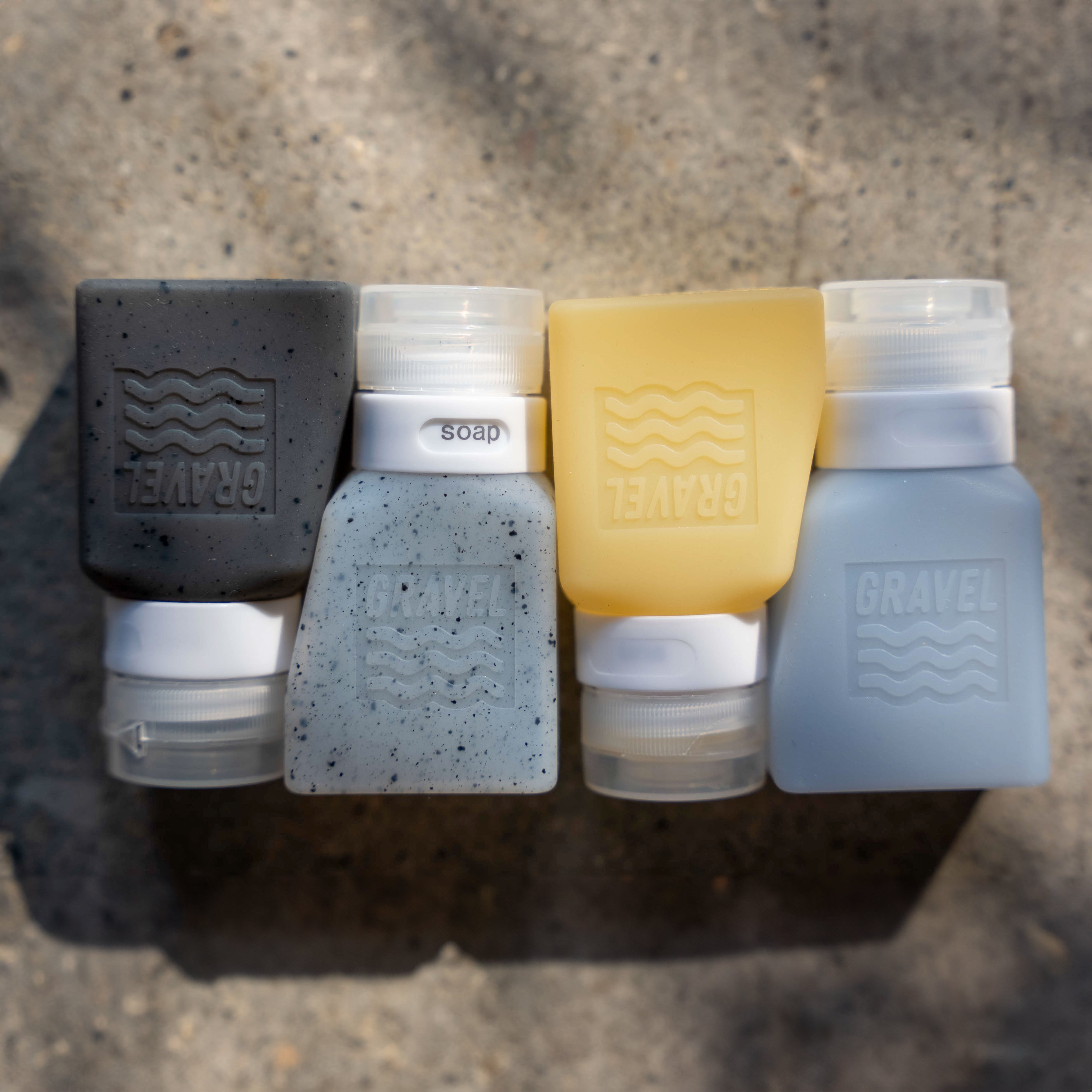 Set of Gravel soap dispensers in various colors on a concrete surface