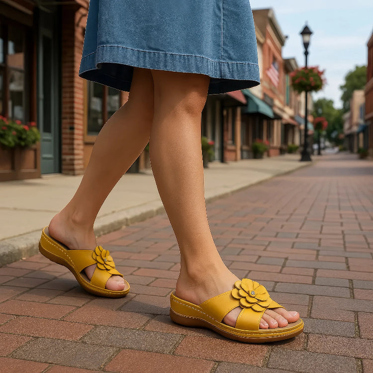 Person wearing yellow sandals with floral designs on a brick sidewalk.