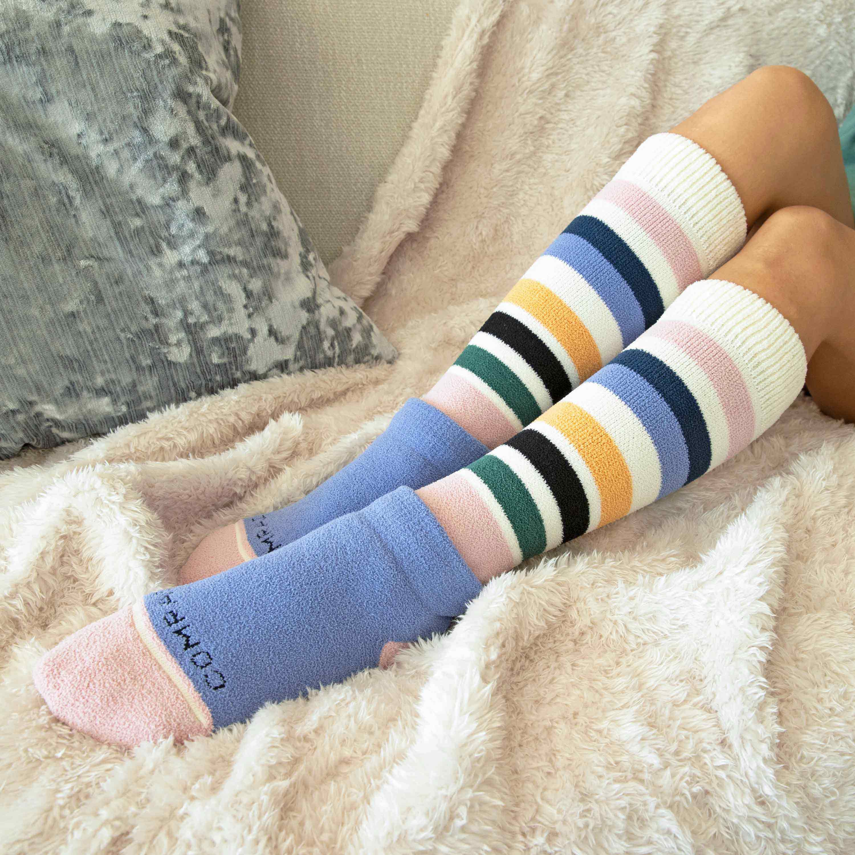 Colorful striped knee-high socks worn by a person sitting on a couch.