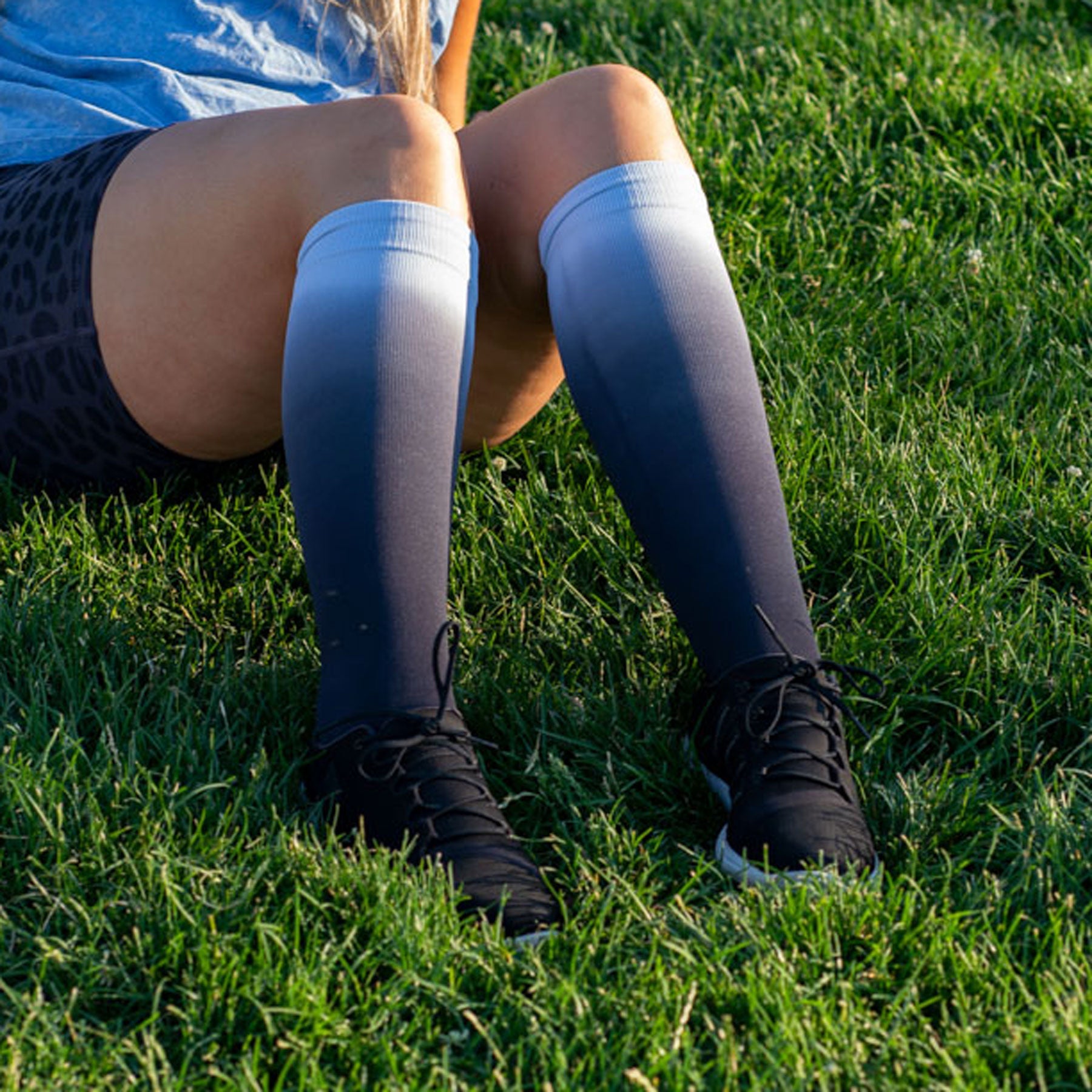 Person sitting on grass wearing knee-high socks and black shoes