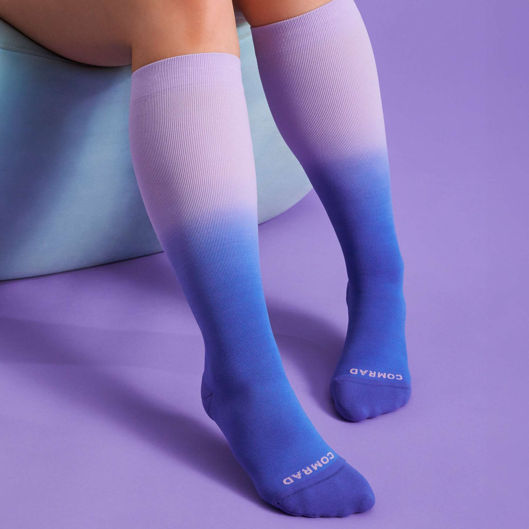 Purple to blue gradient knee-high socks on a person against a purple background