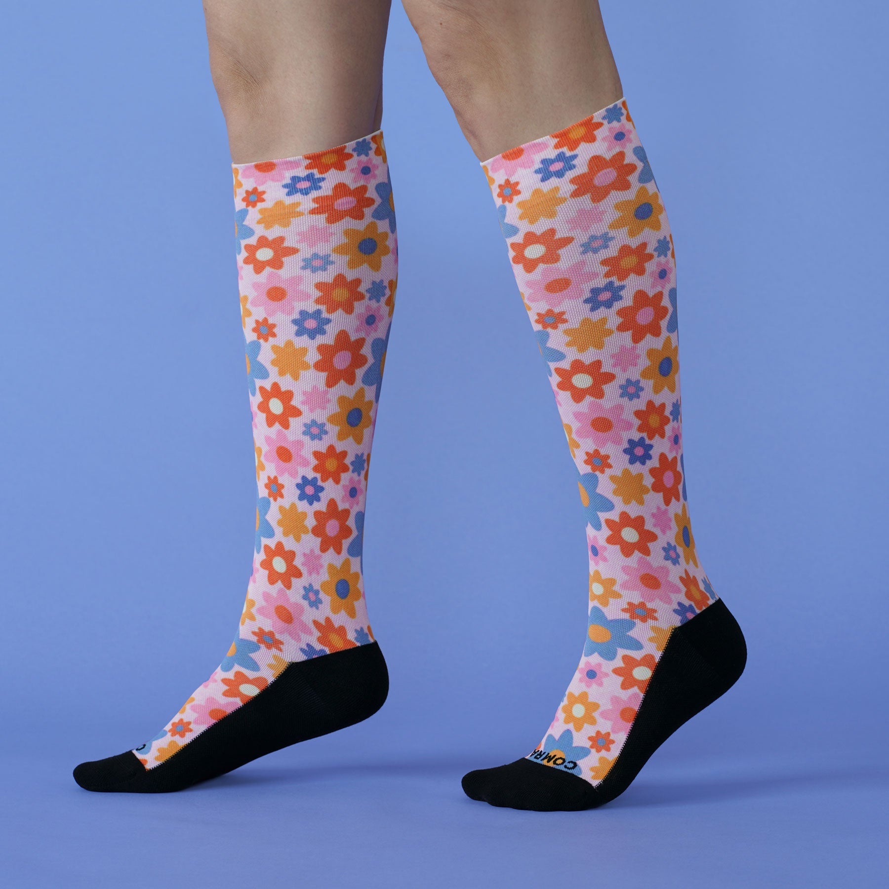 Colorful floral knee-high socks on a person against a blue background