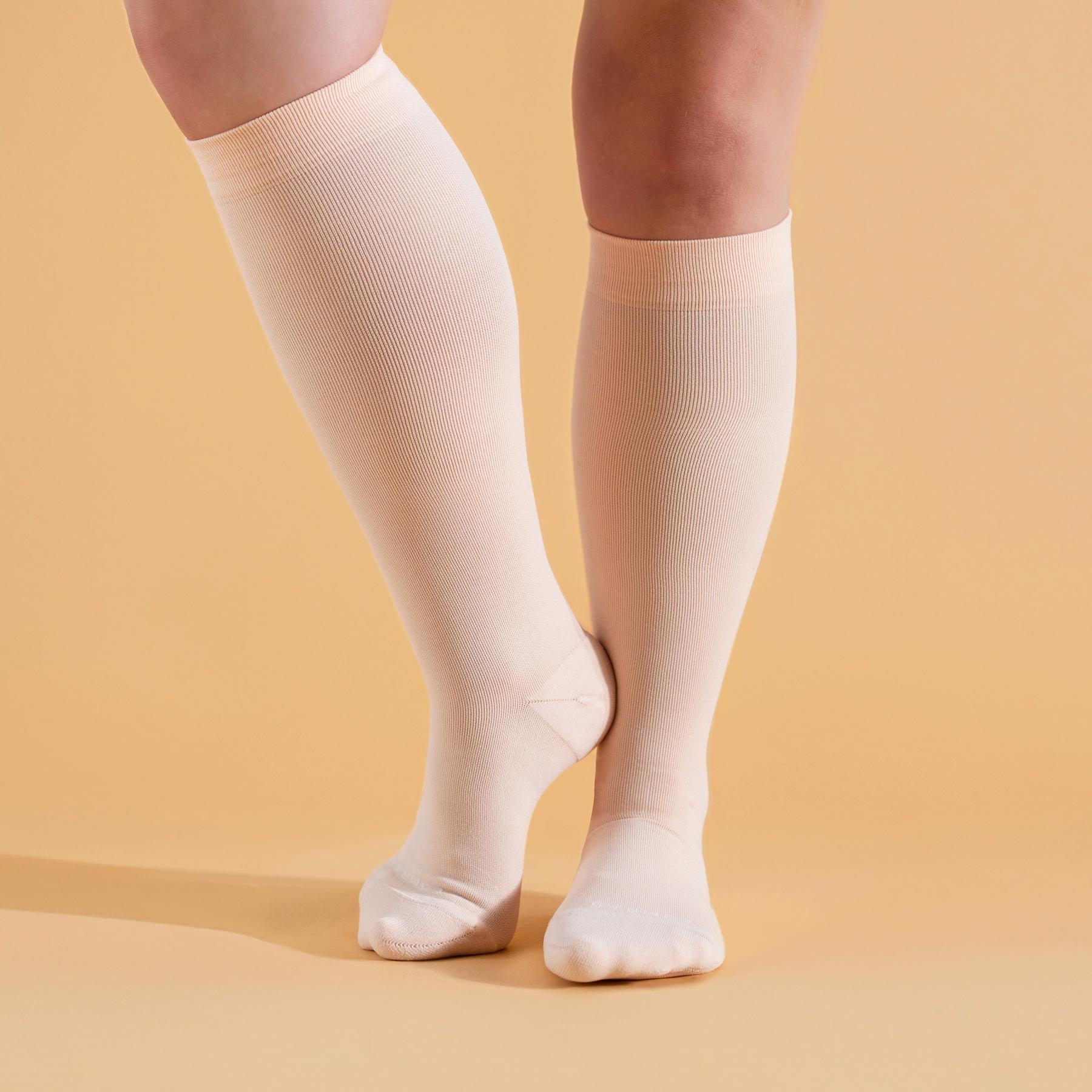 Beige knee-high socks worn by a person on a beige background
