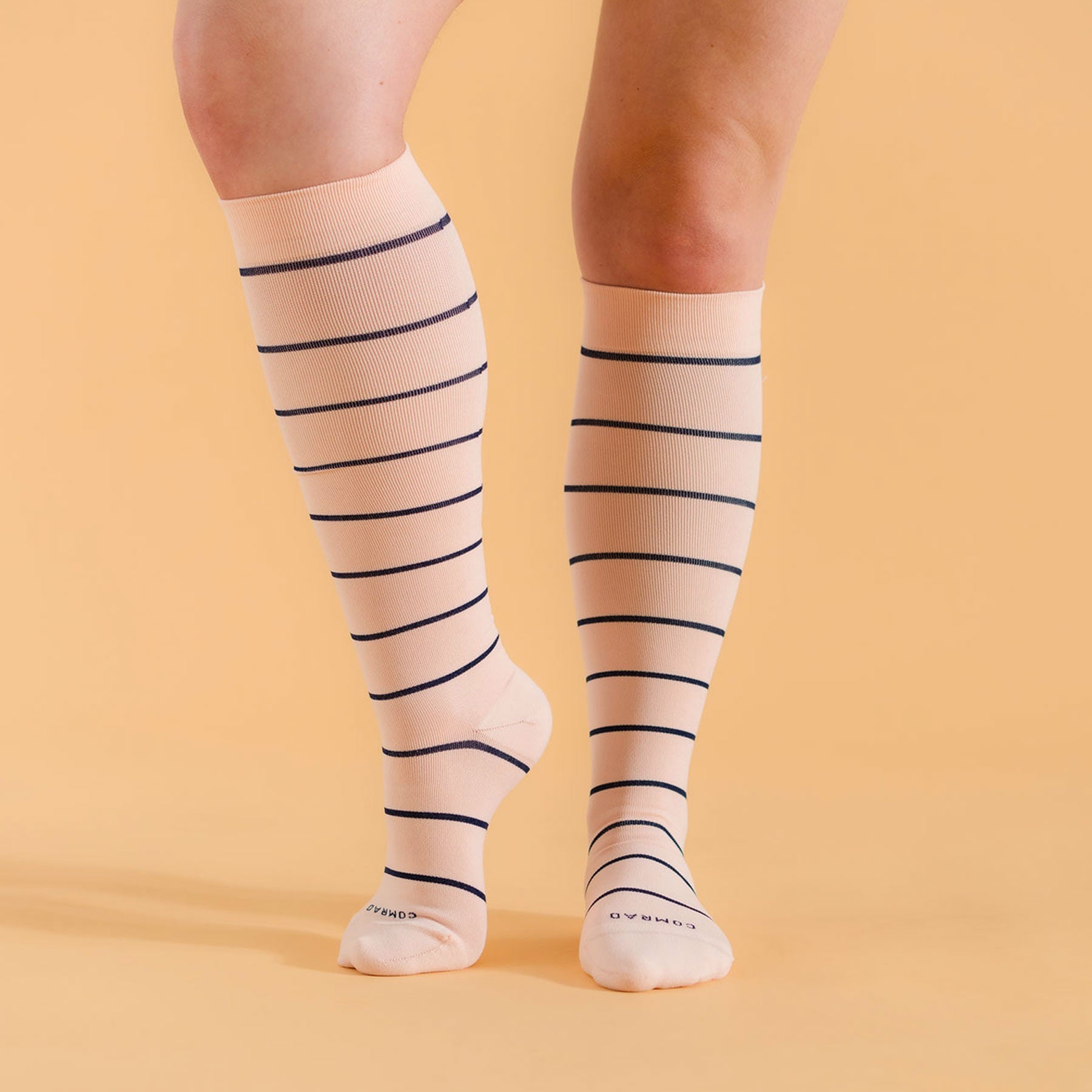 Beige knee-high socks with black stripes worn by a person on a beige background