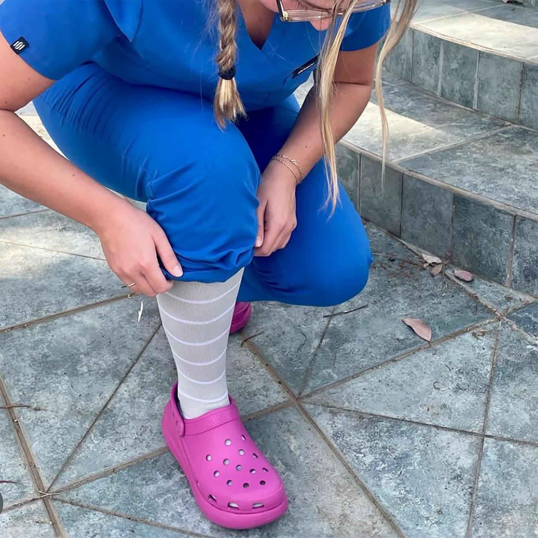 Person wearing blue scrubs and pink Crocs on a stone pavement.