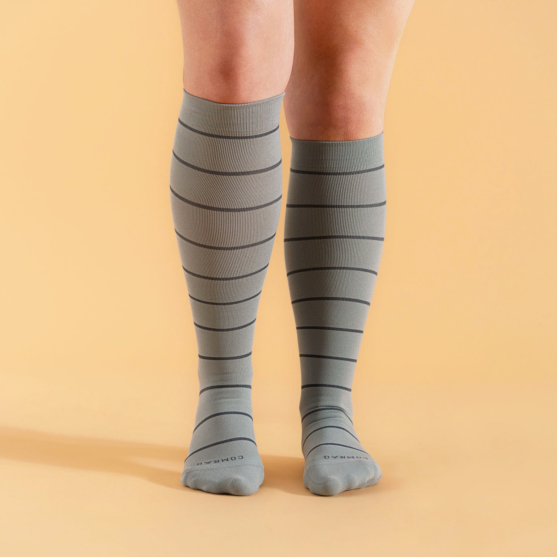 Gray knee-high socks with black stripes worn by a person on an orange background