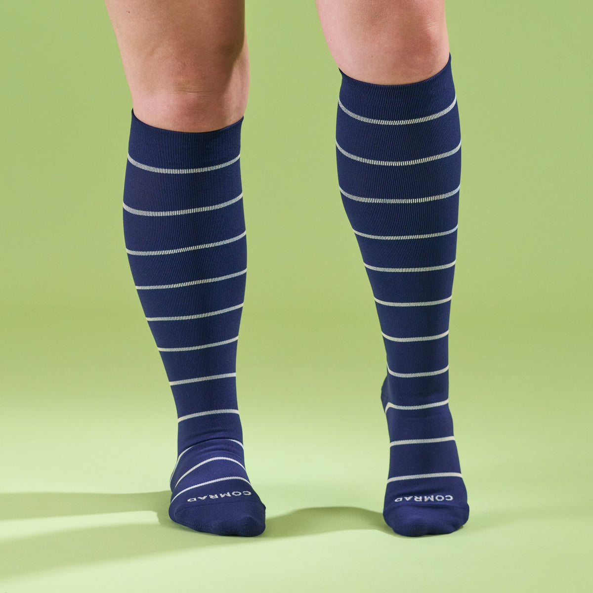 Navy blue knee-high socks with white stripes worn by a person on a green background