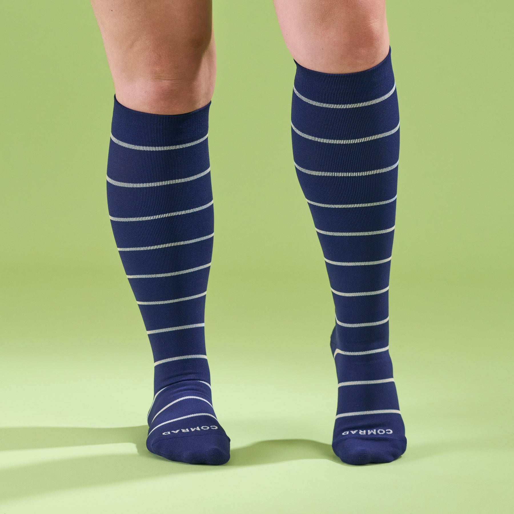 Navy blue knee-high socks with white stripes worn by a person on a green background