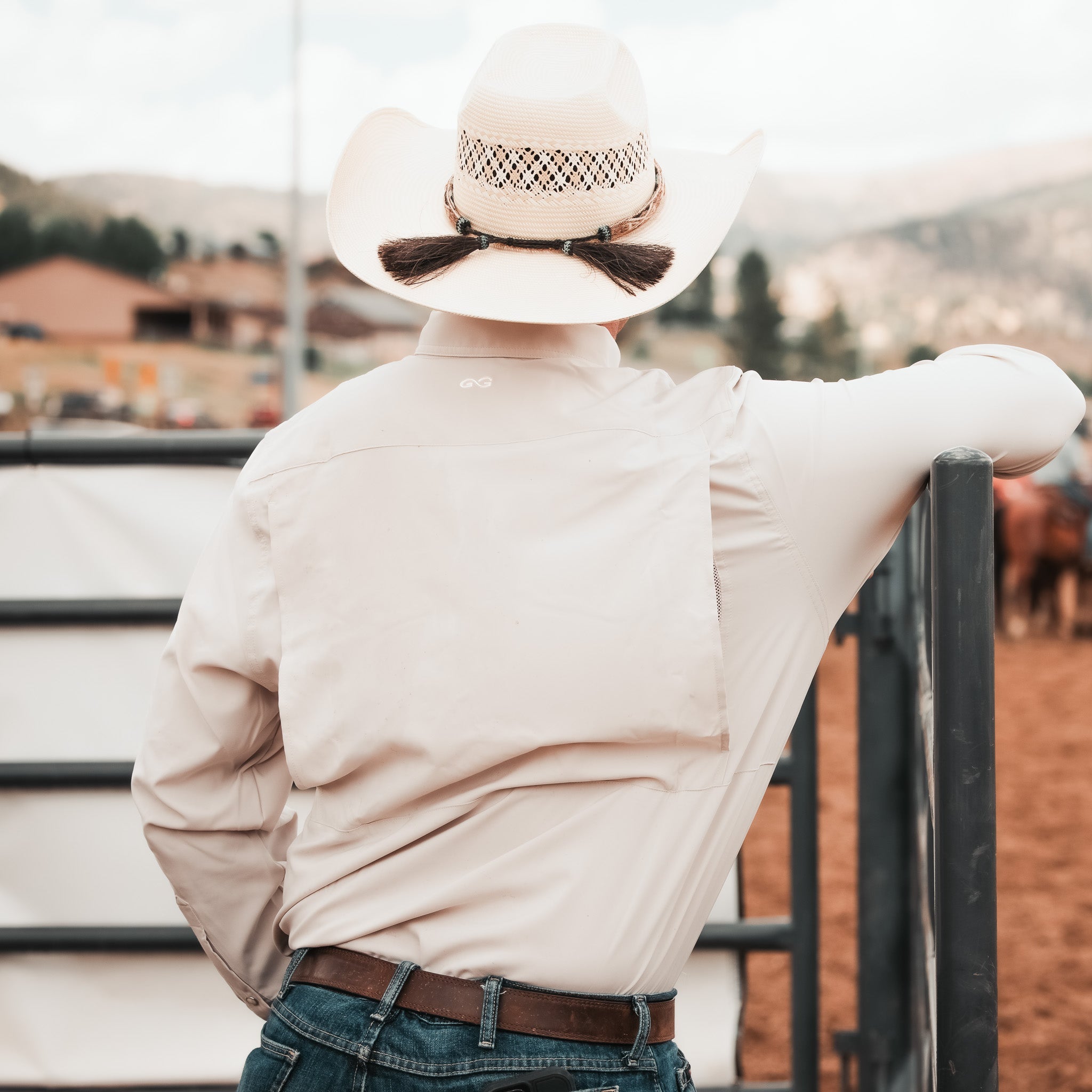 Person wearing a cowboy hat and light-colored shirt, standing with back to camera, in an outdoor setting.