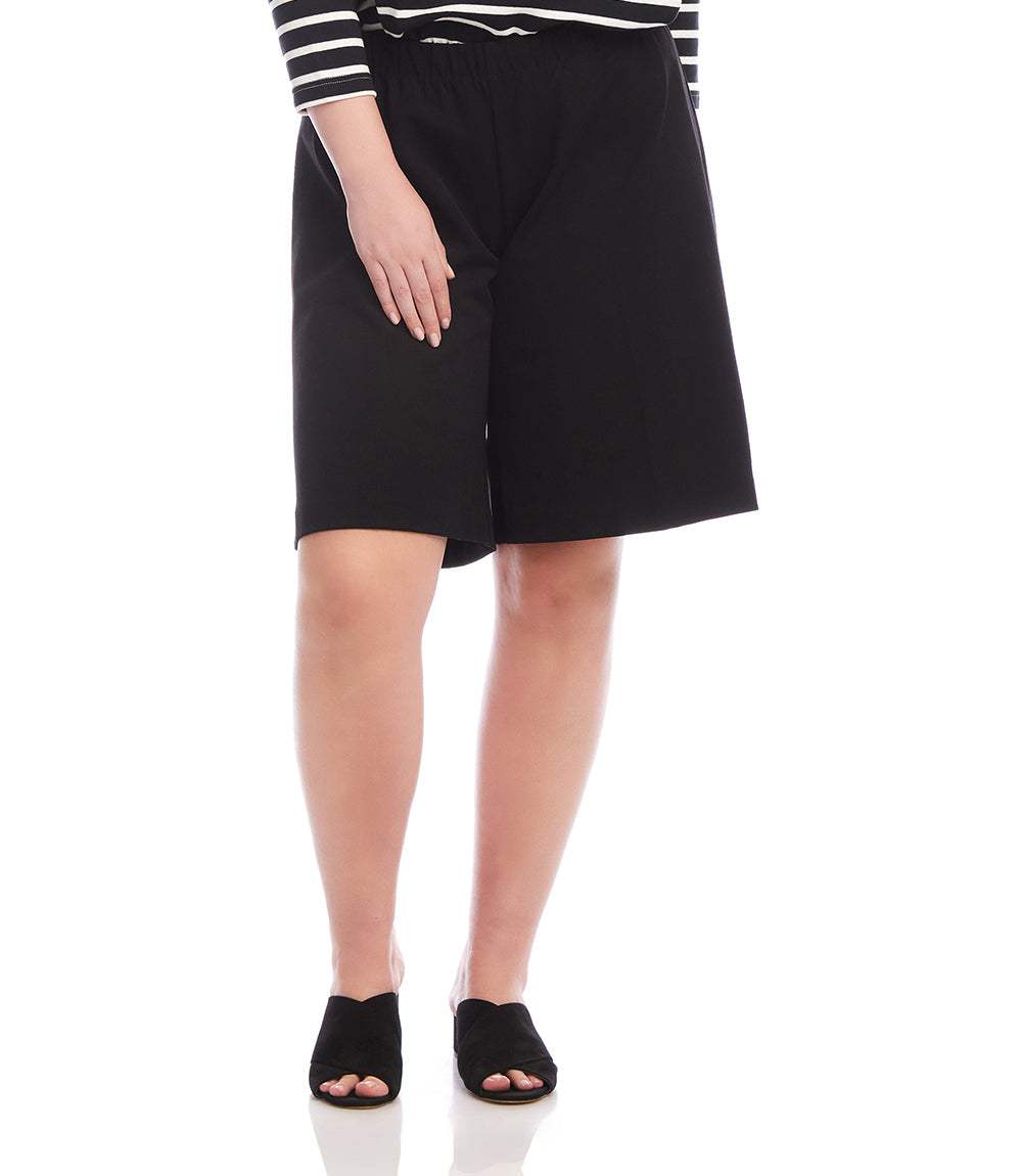 A model wearing black knee-length shorts, a black and white striped long-sleeve top, and black slide sandals, shown from the waist down on a white background.