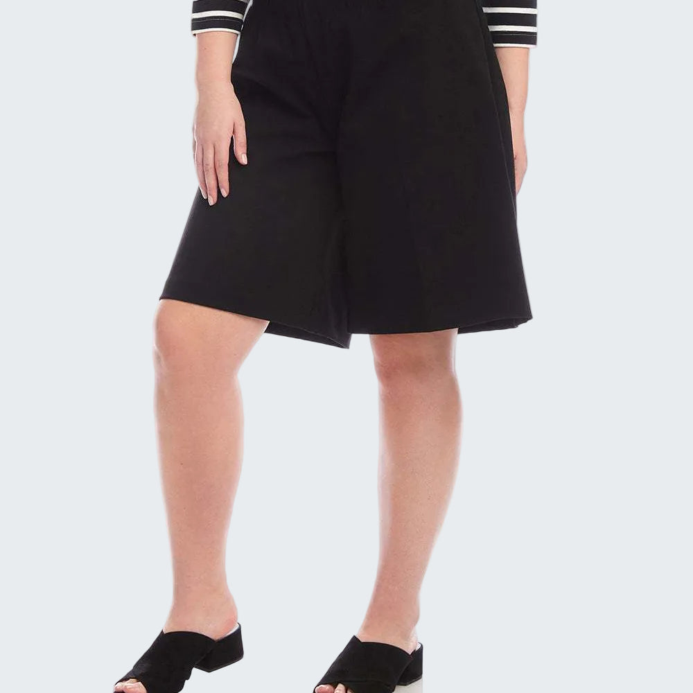 A model wearing black wide-leg shorts, a black and white striped long-sleeve top, and black slide sandals, shown from the waist down on a white studio background.