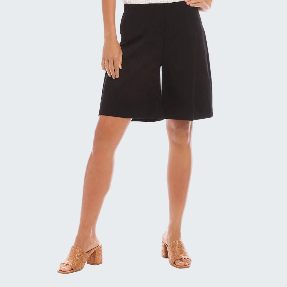 A model wearing black wide-leg shorts and tan block-heel mule sandals against a white studio background.
