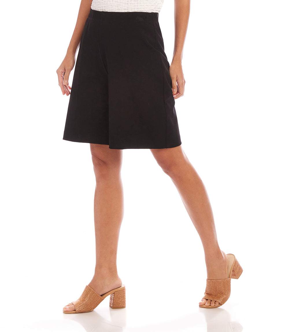 A model wearing a black A-line mini skirt paired with tan block-heel mule sandals against a clean white studio background.
