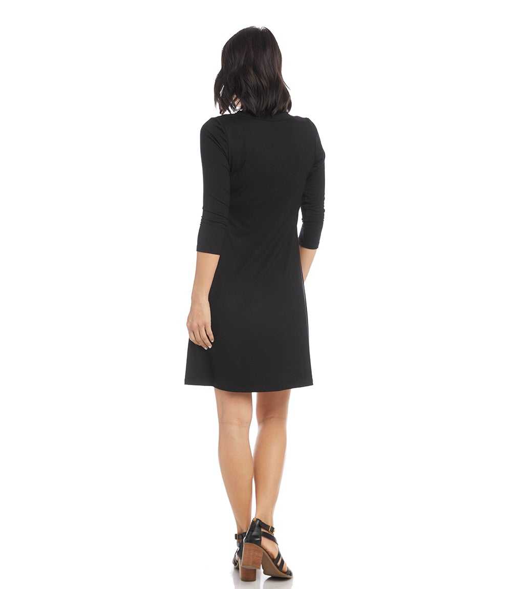 A woman viewed from the back wearing a black knee-length dress with three-quarter sleeves and brown strappy heels, against a plain white background.