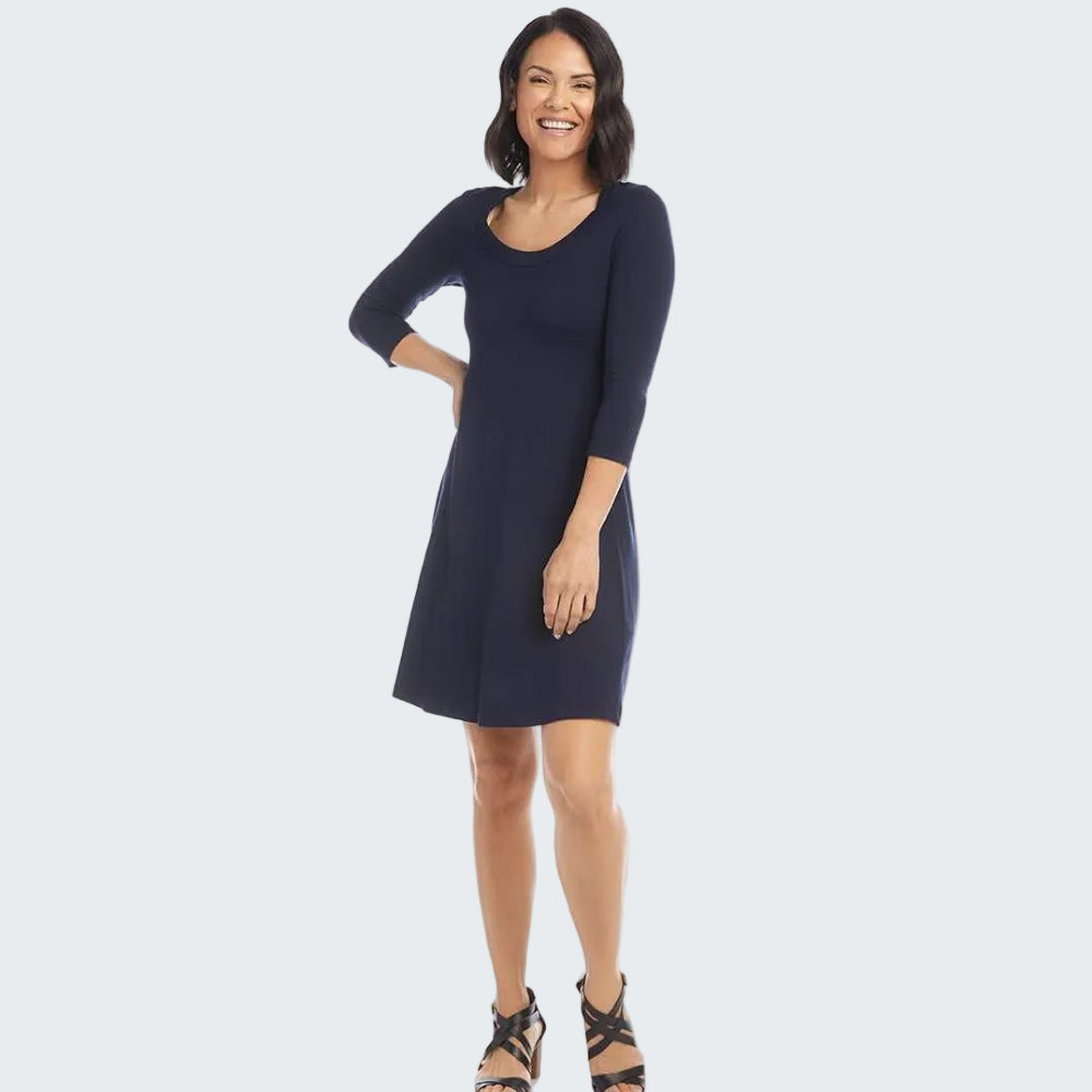 A woman modeling a navy blue three-quarter sleeve shift dress with a scoop neckline, paired with black strappy sandals, against a solid white background.