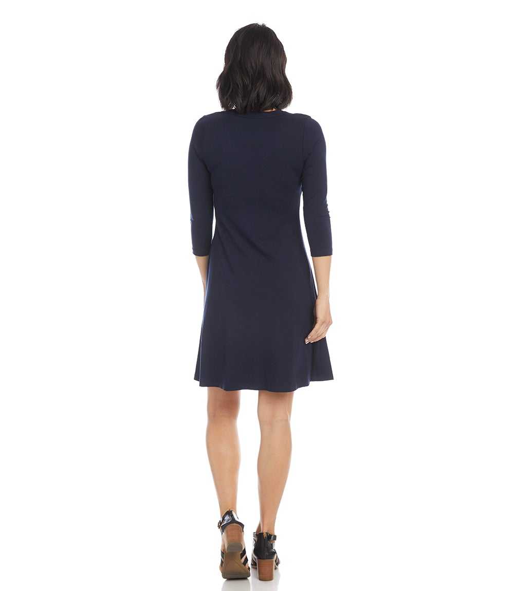 A woman viewed from the back wearing a dark navy knee-length dress with three-quarter sleeves and brown platform sandals, set against a plain white background.