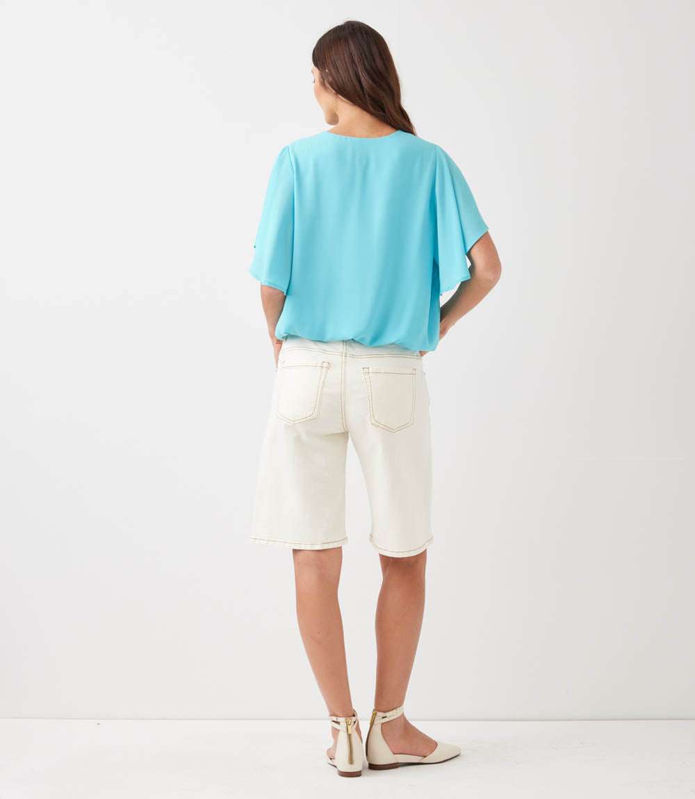 Woman wearing a light blue top and white shorts on a white background