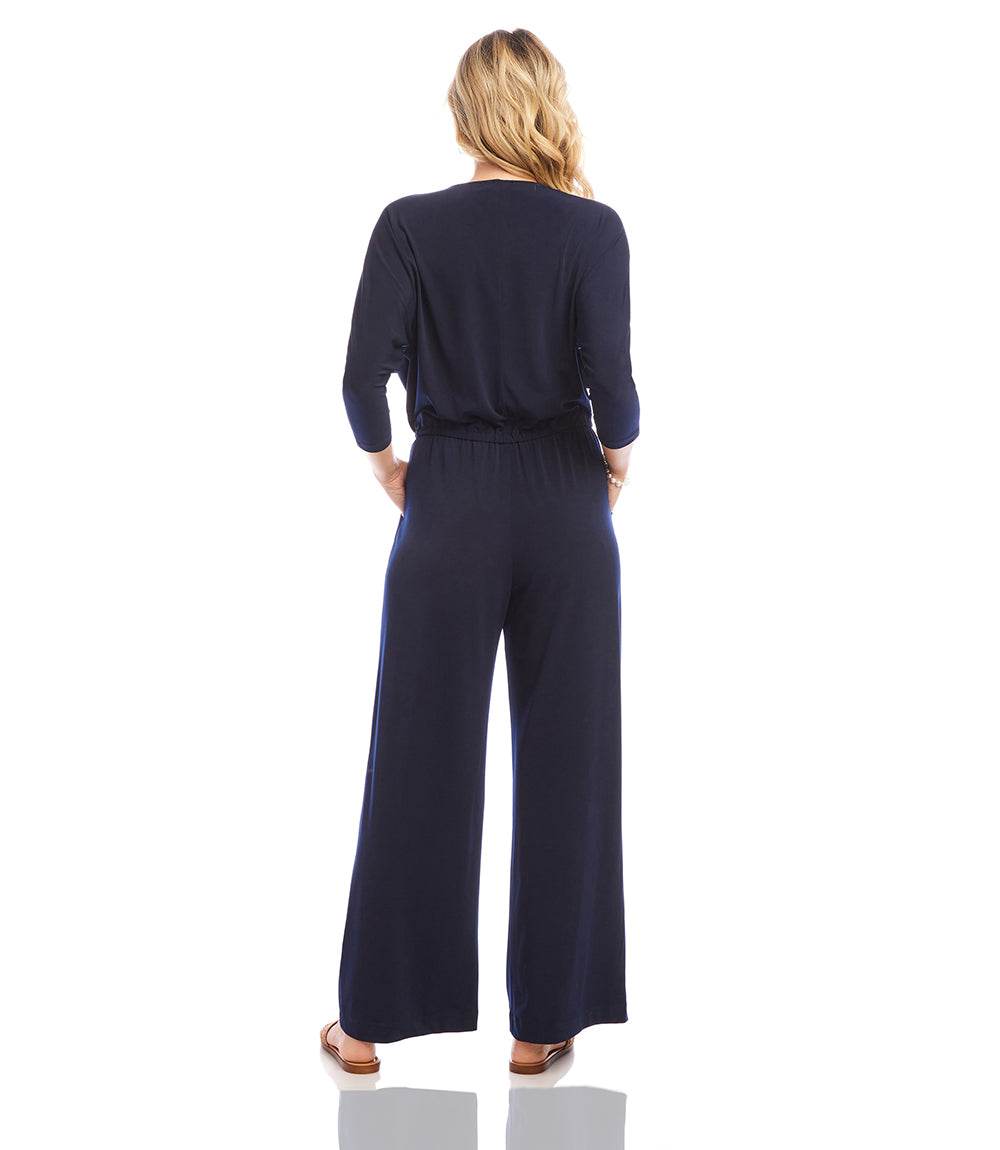 A woman viewed from behind wearing a navy blue three-quarter sleeve jumpsuit with wide legs, standing against a plain white background.