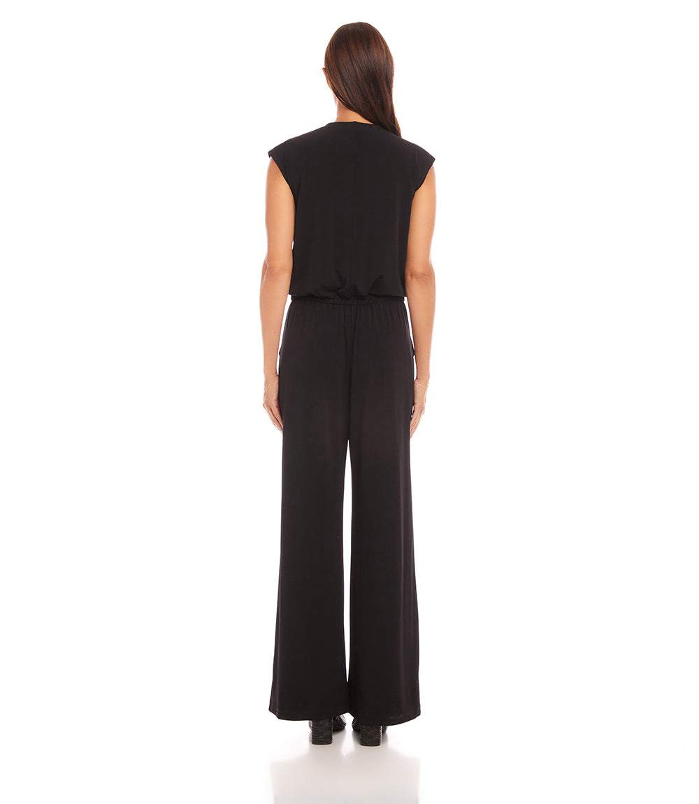 A woman viewed from the back wearing a black sleeveless jumpsuit with wide legs, standing against a plain white studio background.