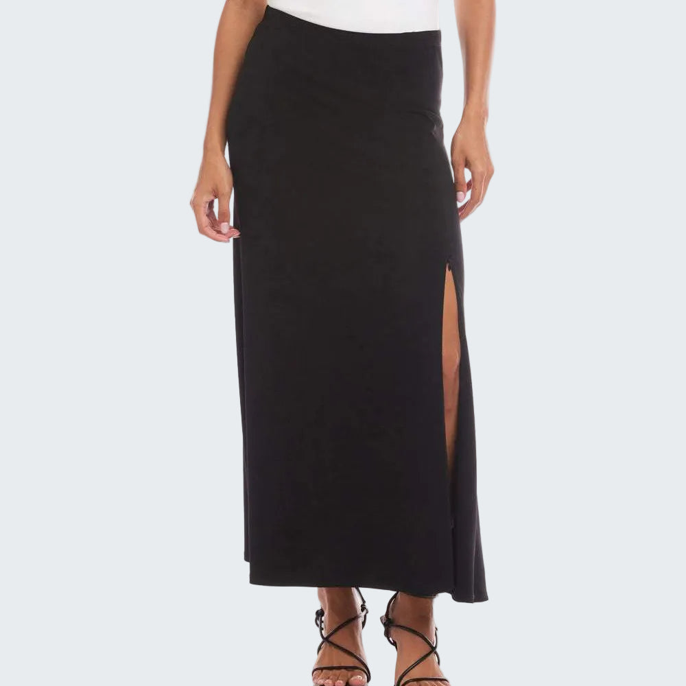 A model wearing a black maxi skirt with a high side slit, paired with a white top and black strappy sandals, shown against a plain white studio background.