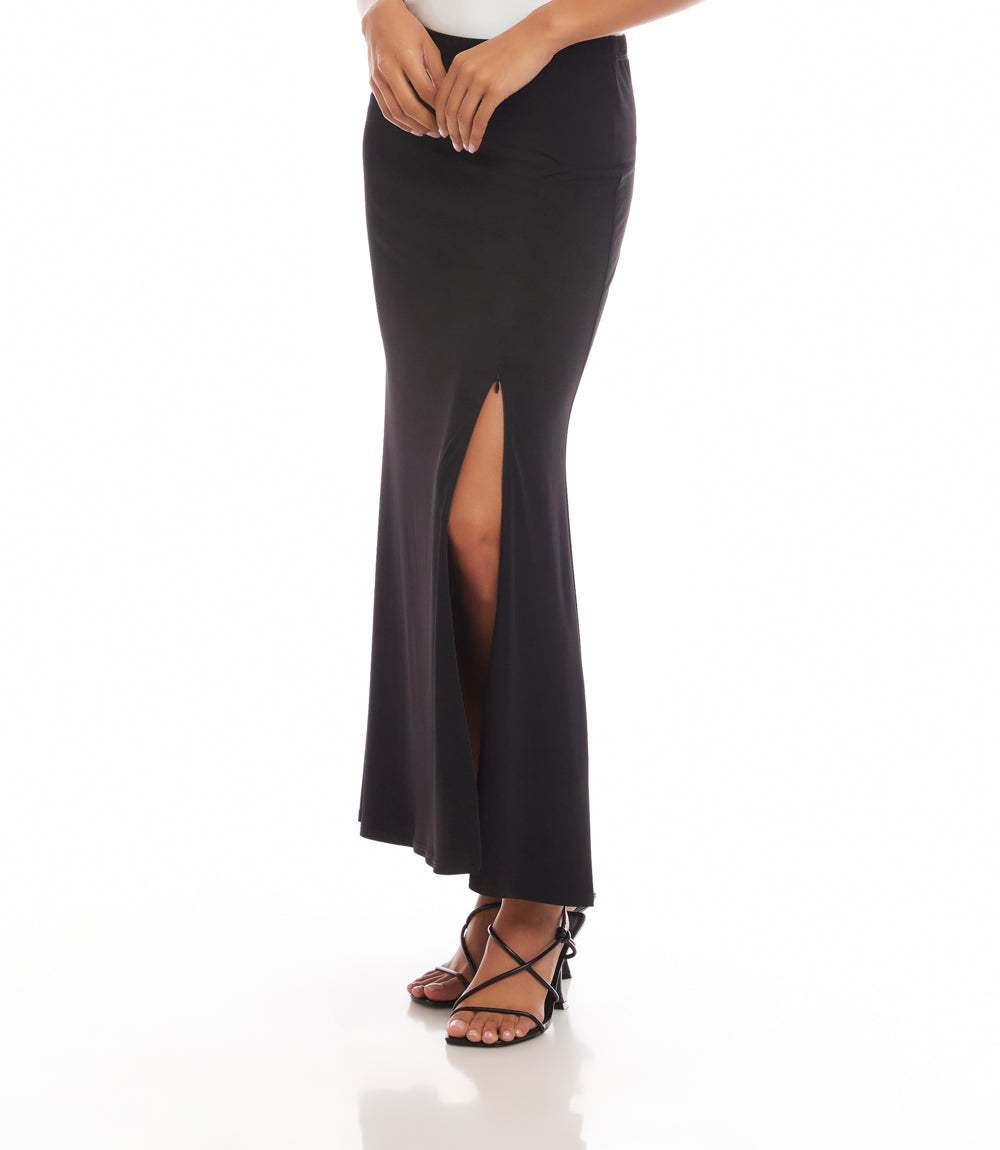 A woman wearing a black high-waisted maxi skirt with a front slit, paired with black strappy high-heeled sandals, shown against a plain white studio background.