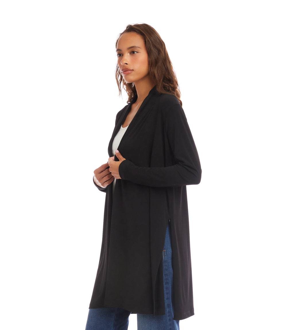 A woman modeling a black long-sleeve open-front cardigan over a white top and blue jeans, photographed against a plain white studio background.