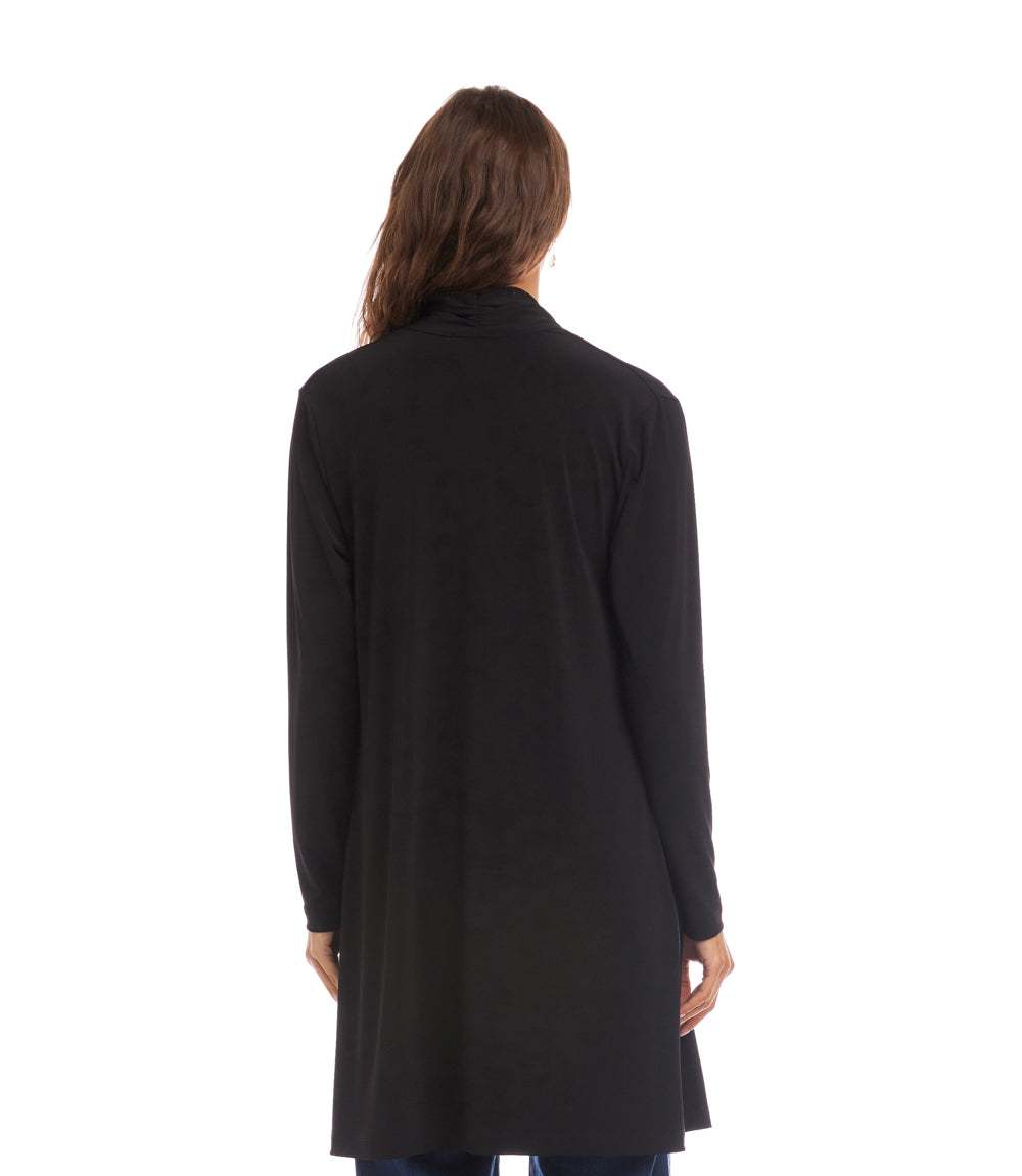 A woman viewed from the back wearing a long-sleeve black tunic or longline cardigan, photographed against a plain white studio background.