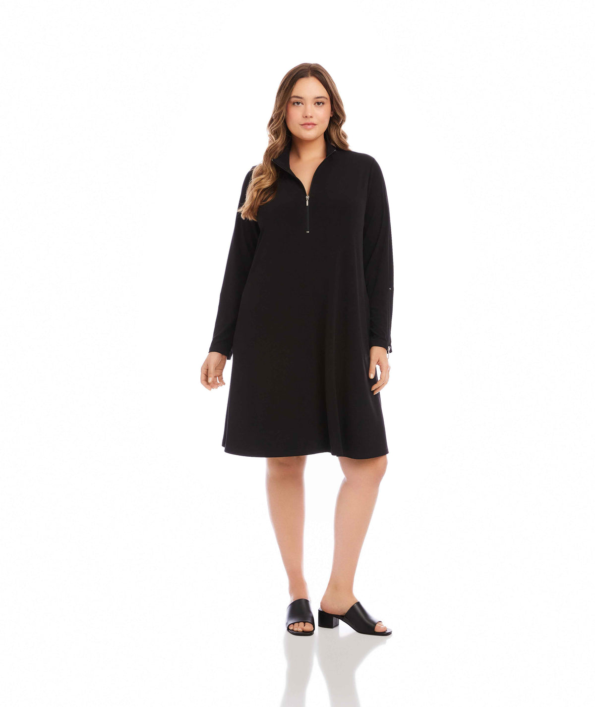 A woman modeling a black long-sleeve shift dress with a half-zip collar, photographed against a seamless white studio background.