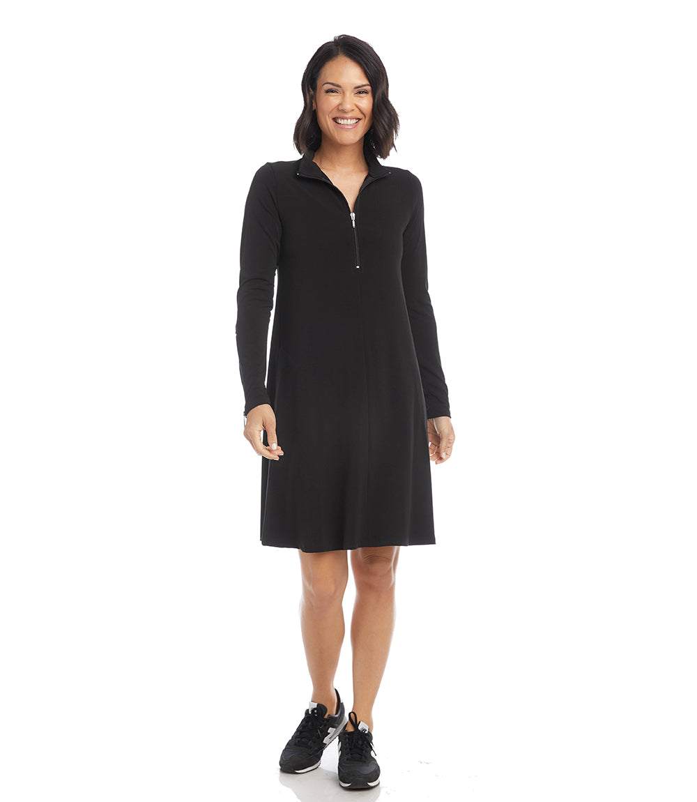 A woman modeling a black long-sleeve shift dress with a half-zip mock neck, standing against a plain white background.