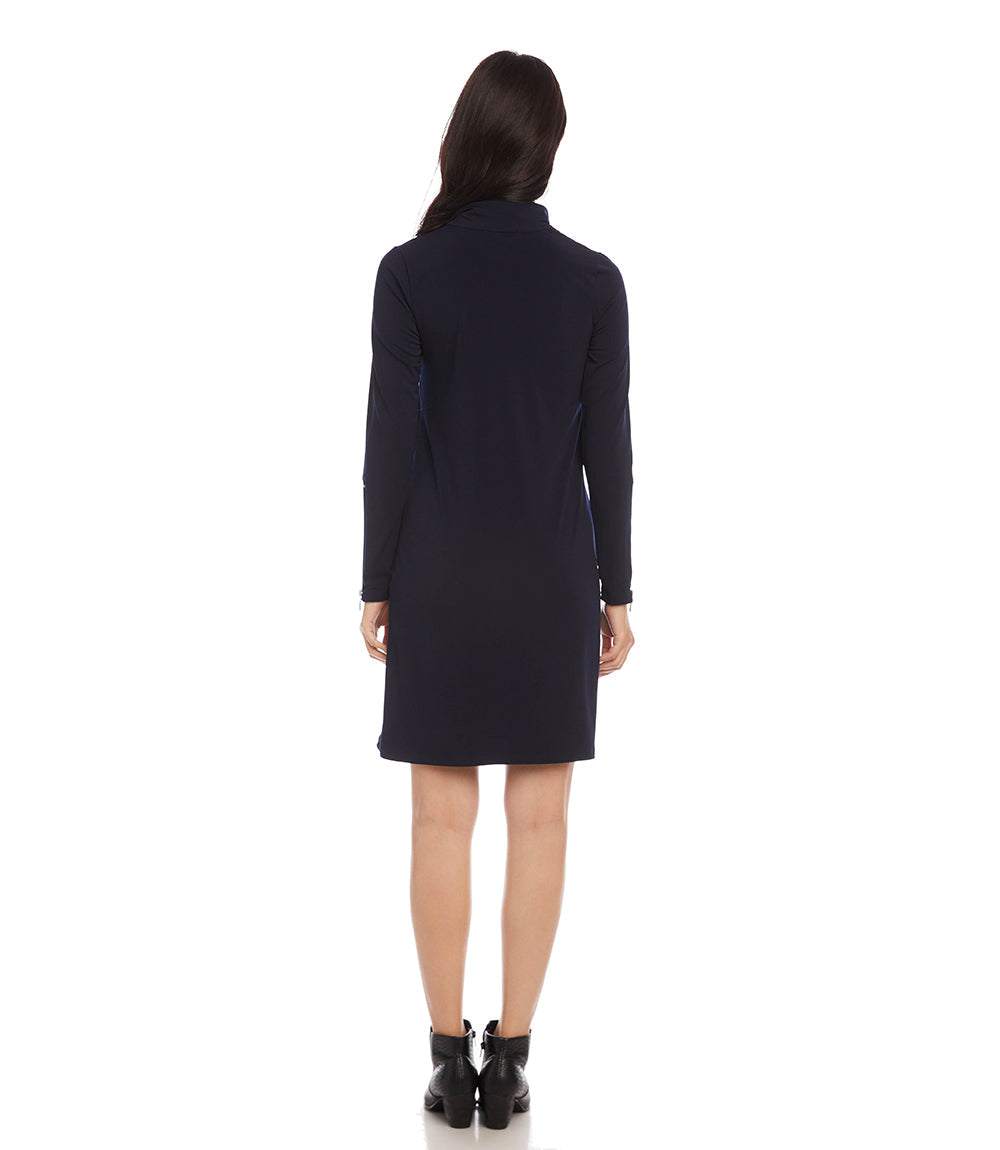 A woman viewed from the back wearing a dark navy long-sleeve dress with a high collar and black ankle boots, set against a plain white background.