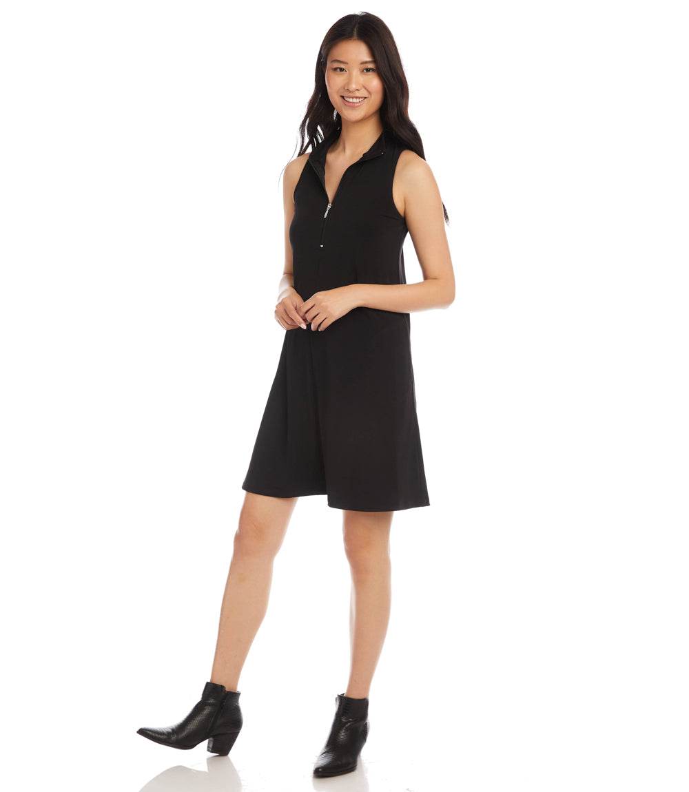 A woman modeling a sleeveless black mini dress with a V-neckline and button-front detail, paired with black ankle boots, against a plain white studio background.