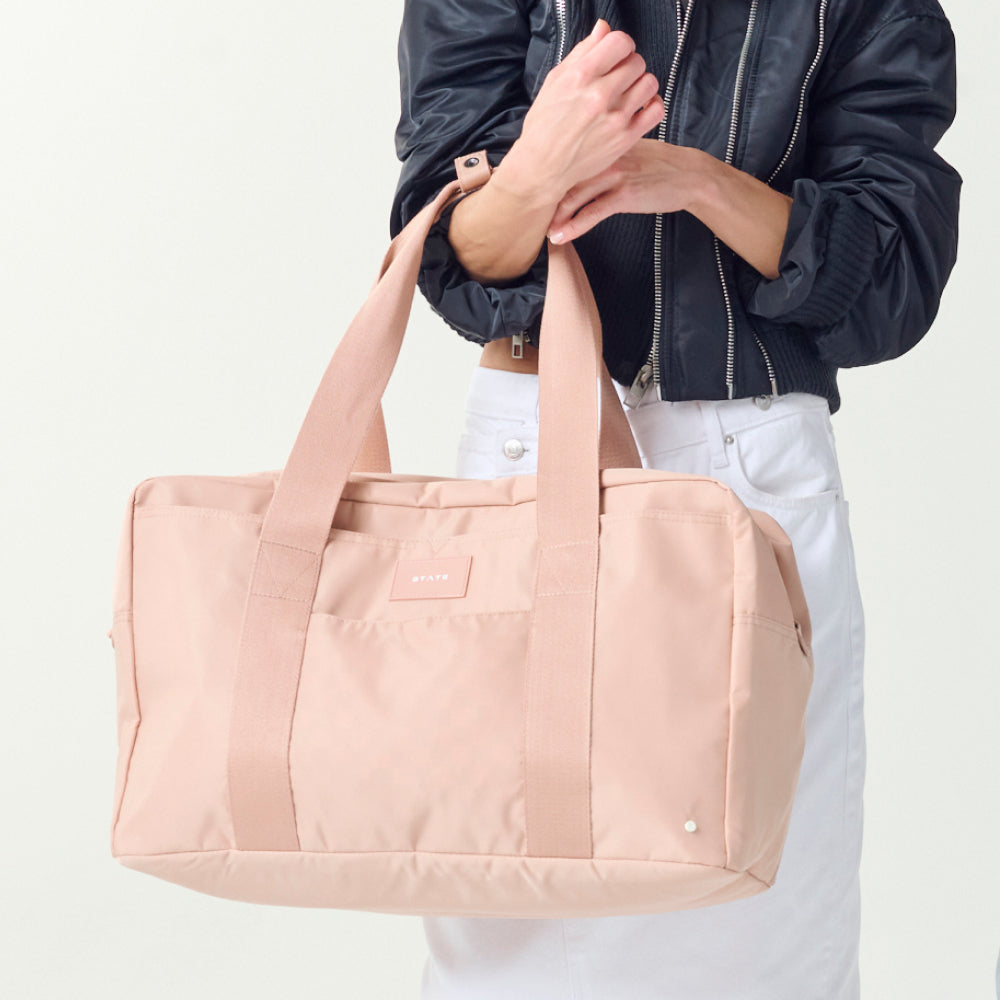 Person holding a pink duffel bag against a white background