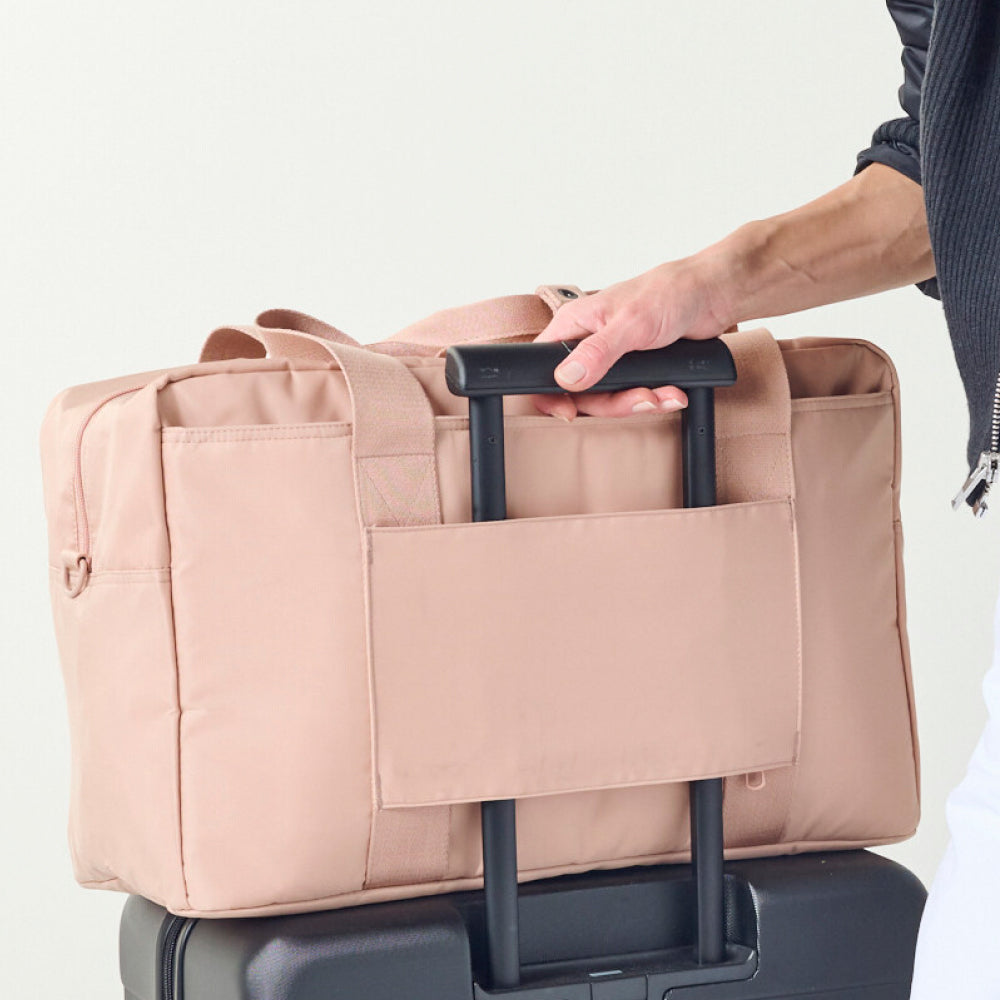 Person holding a beige duffel bag with black handles on a light gray background