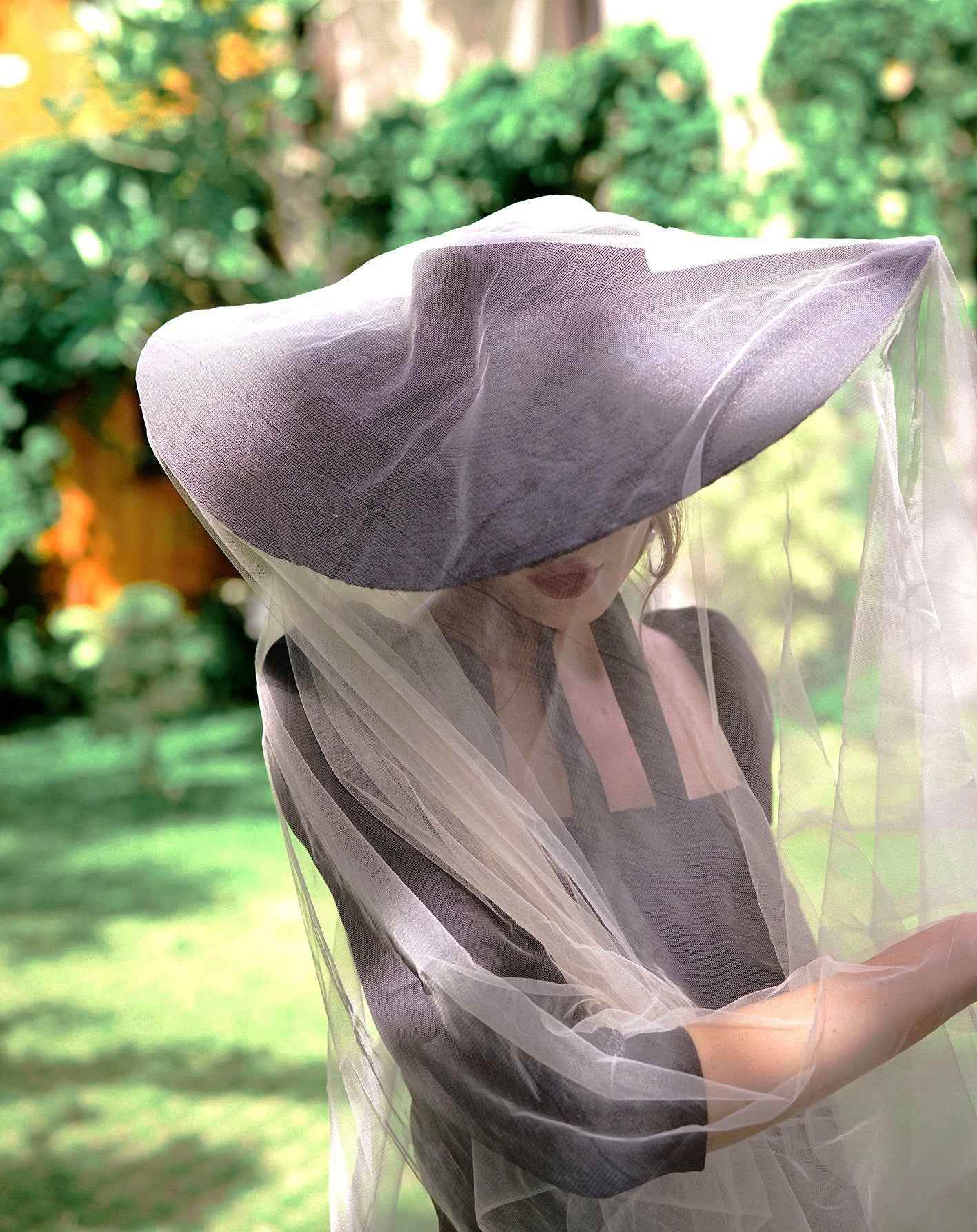 Person wearing a wide-brimmed hat and veil in a garden setting