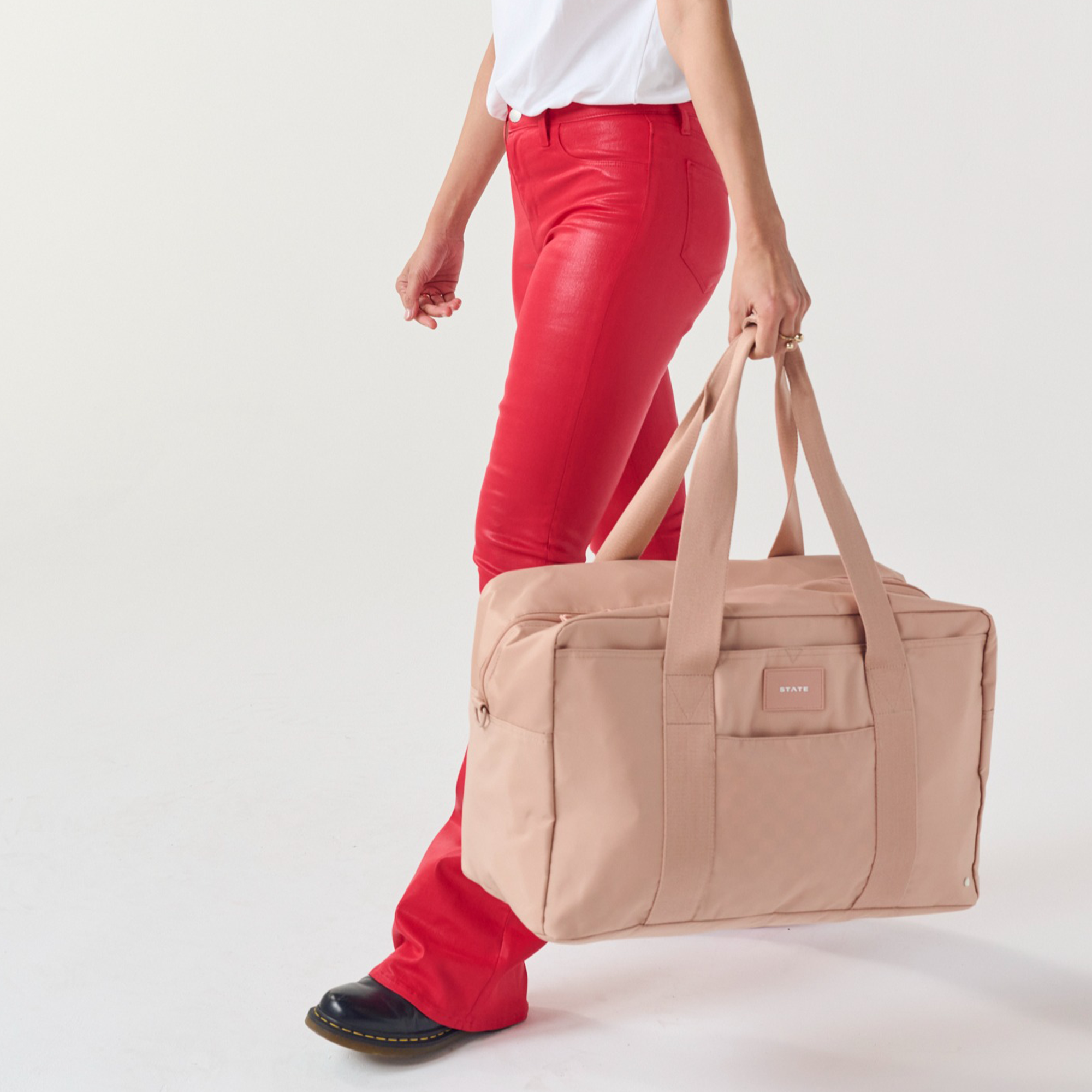 Person holding a beige duffel bag with a plain background