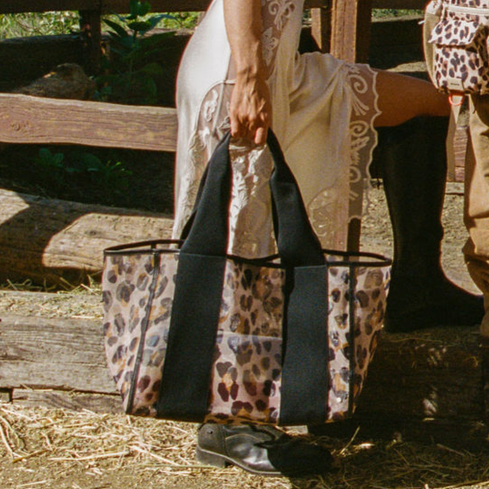 Person holding a black bag with leopard print accents in a rustic outdoor setting.