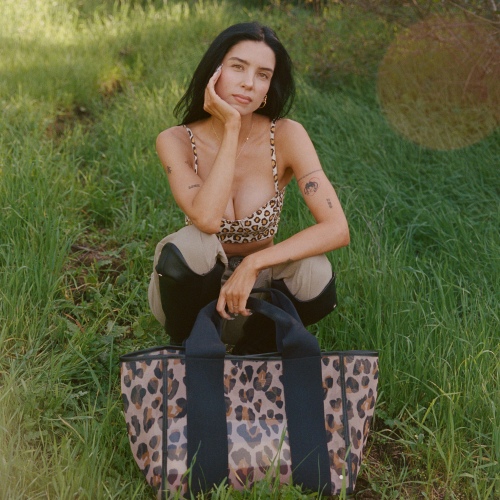 Woman sitting in a grassy field with a leopard print bag