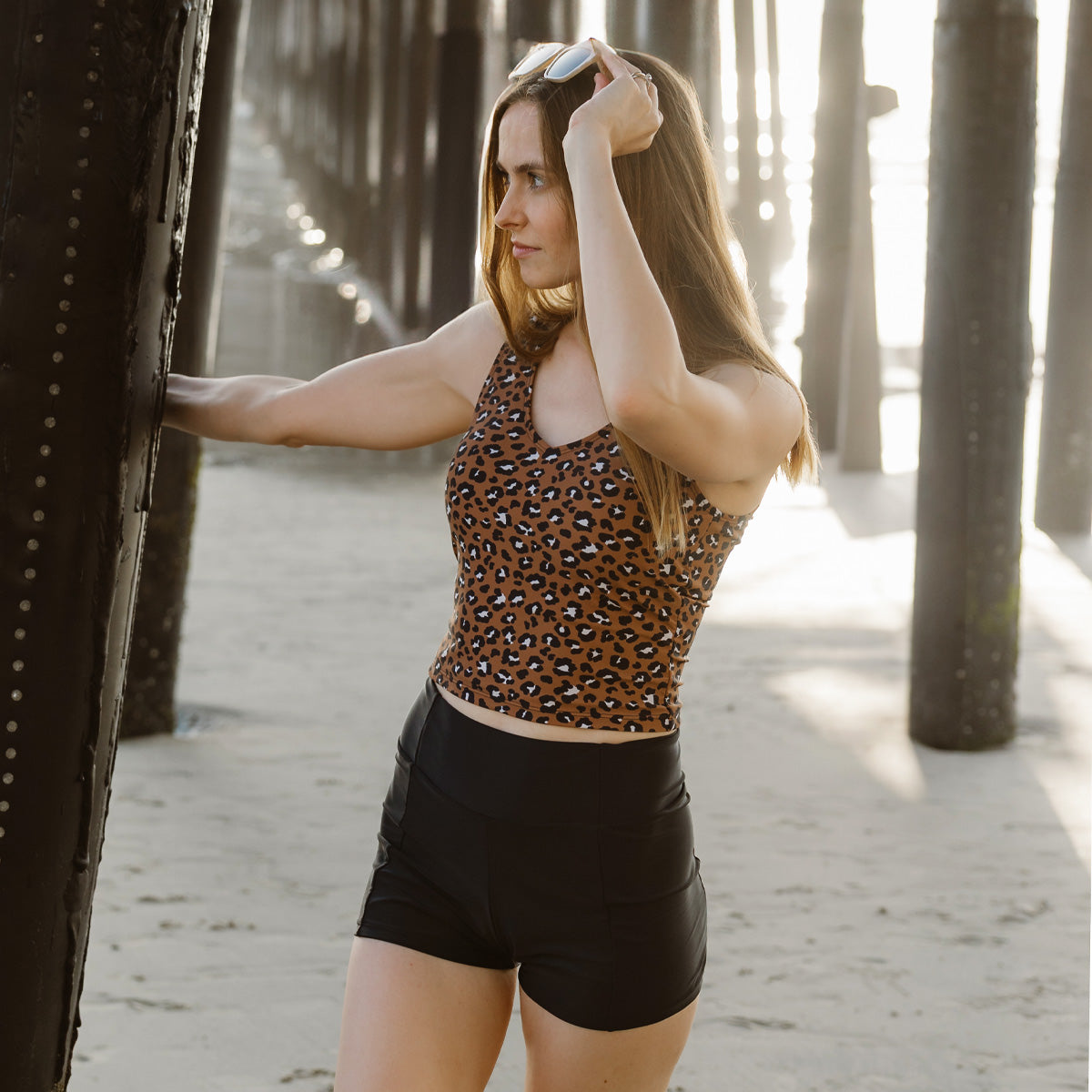 Woman in a leopard print top and black shorts standing on a wooden pier.