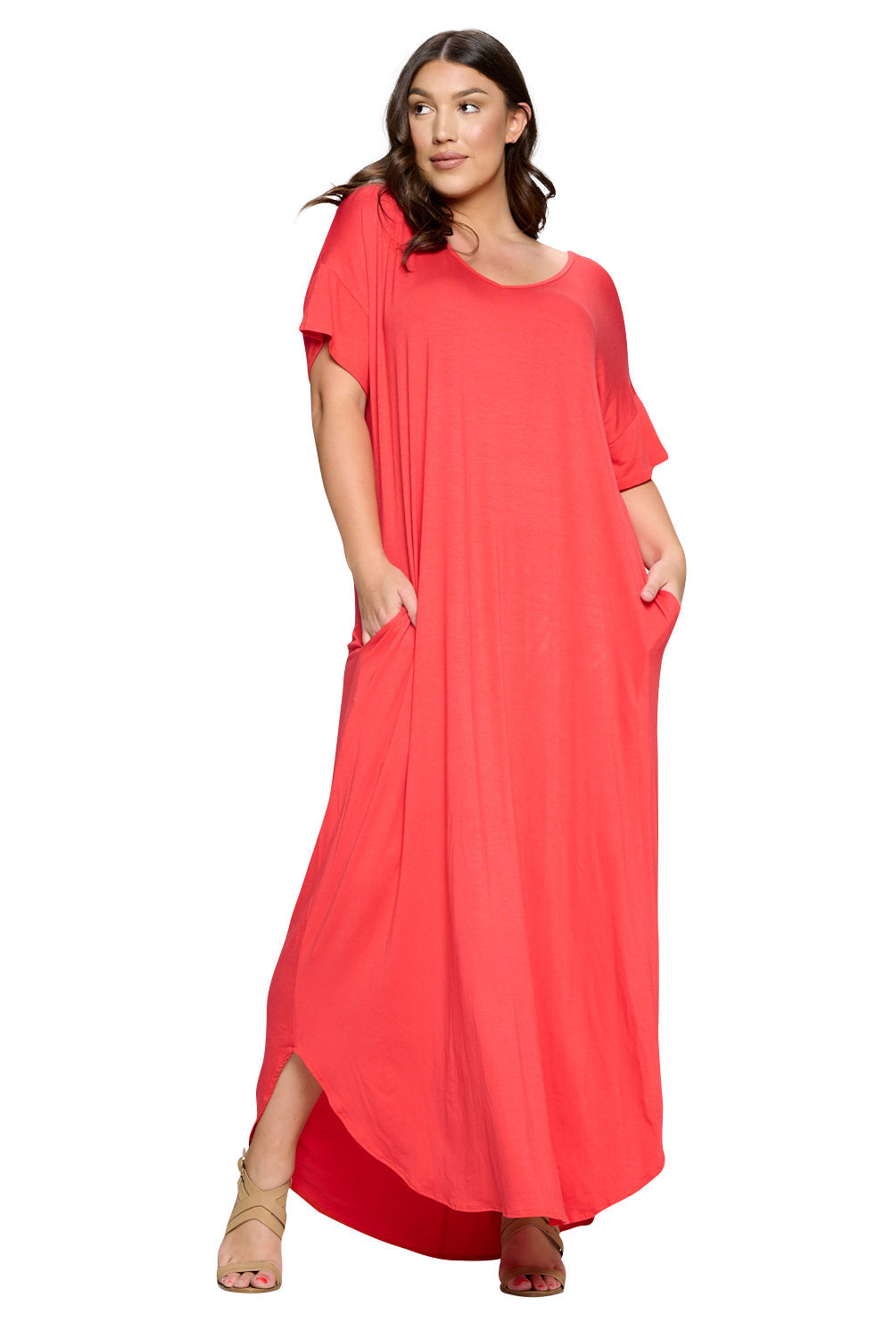 A woman modeling a loose, coral-red maxi dress with short sleeves, side pockets, and a draped silhouette, photographed against a plain white background.