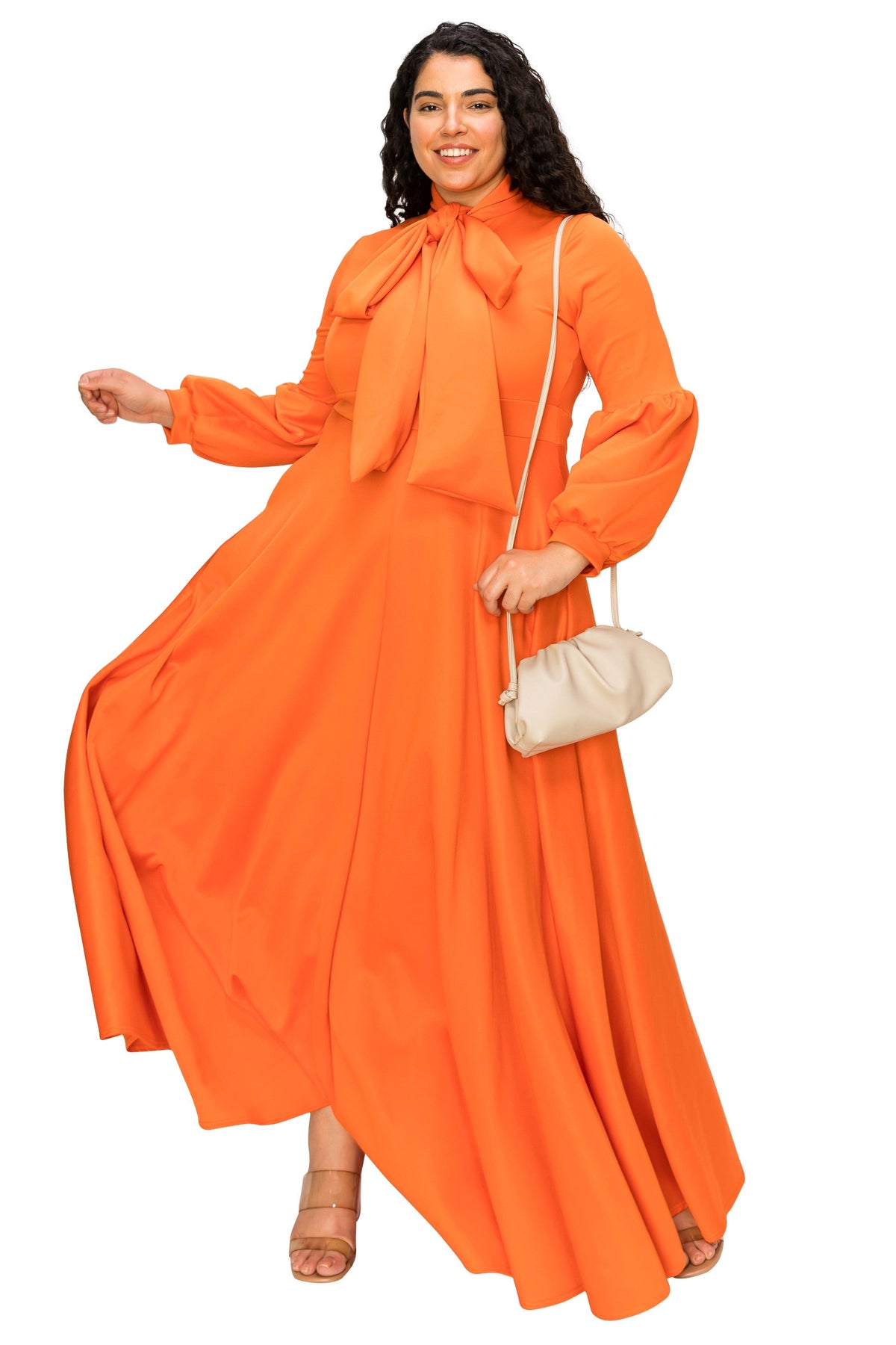 A woman modeling a bright orange long-sleeve maxi dress with a high neck and large bow detail, holding a small cream-colored handbag against a plain white background.