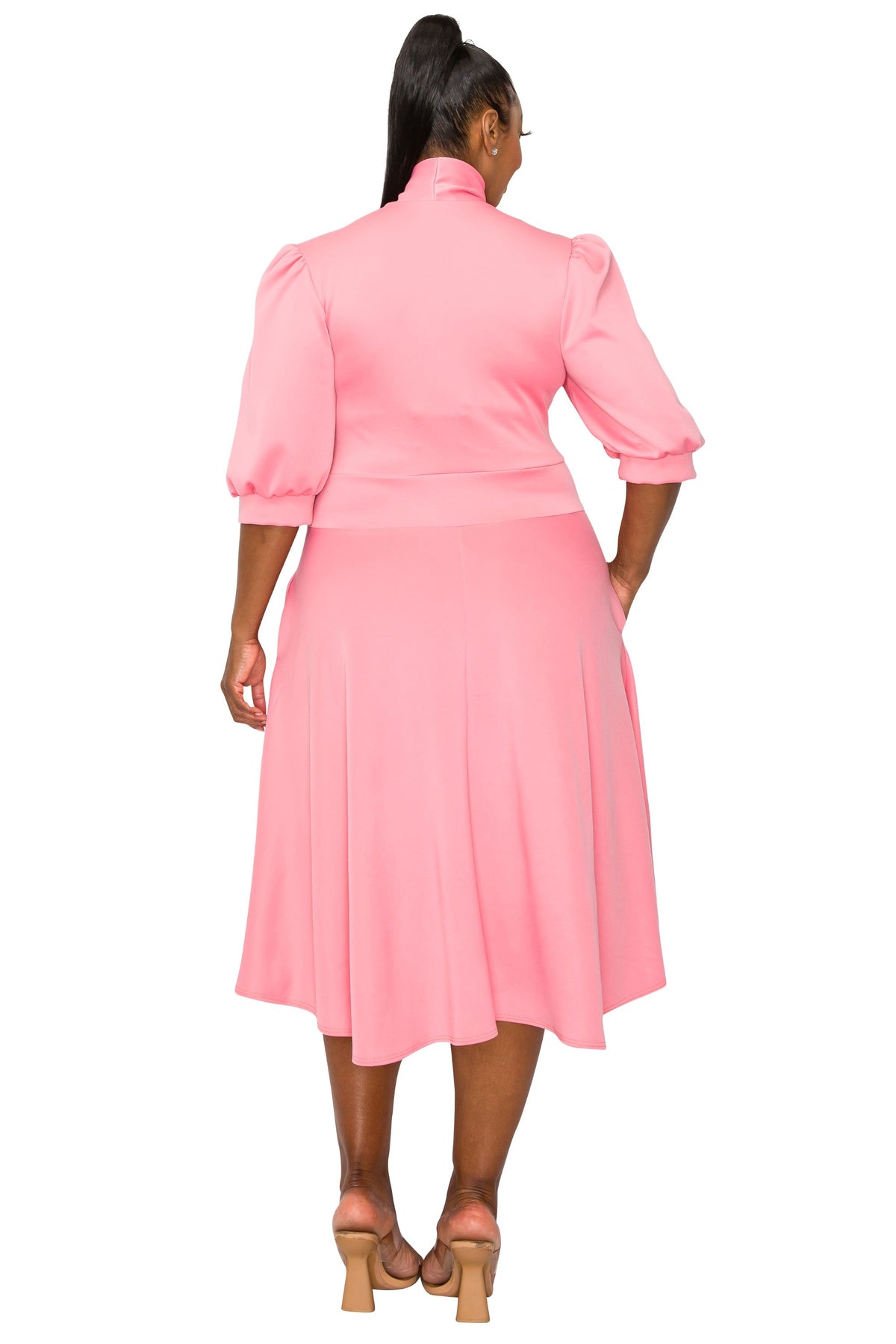A woman viewed from the back wearing a pink midi dress with puff sleeves, a high mock neck, and a flared skirt, paired with tan heeled sandals against a plain white background.