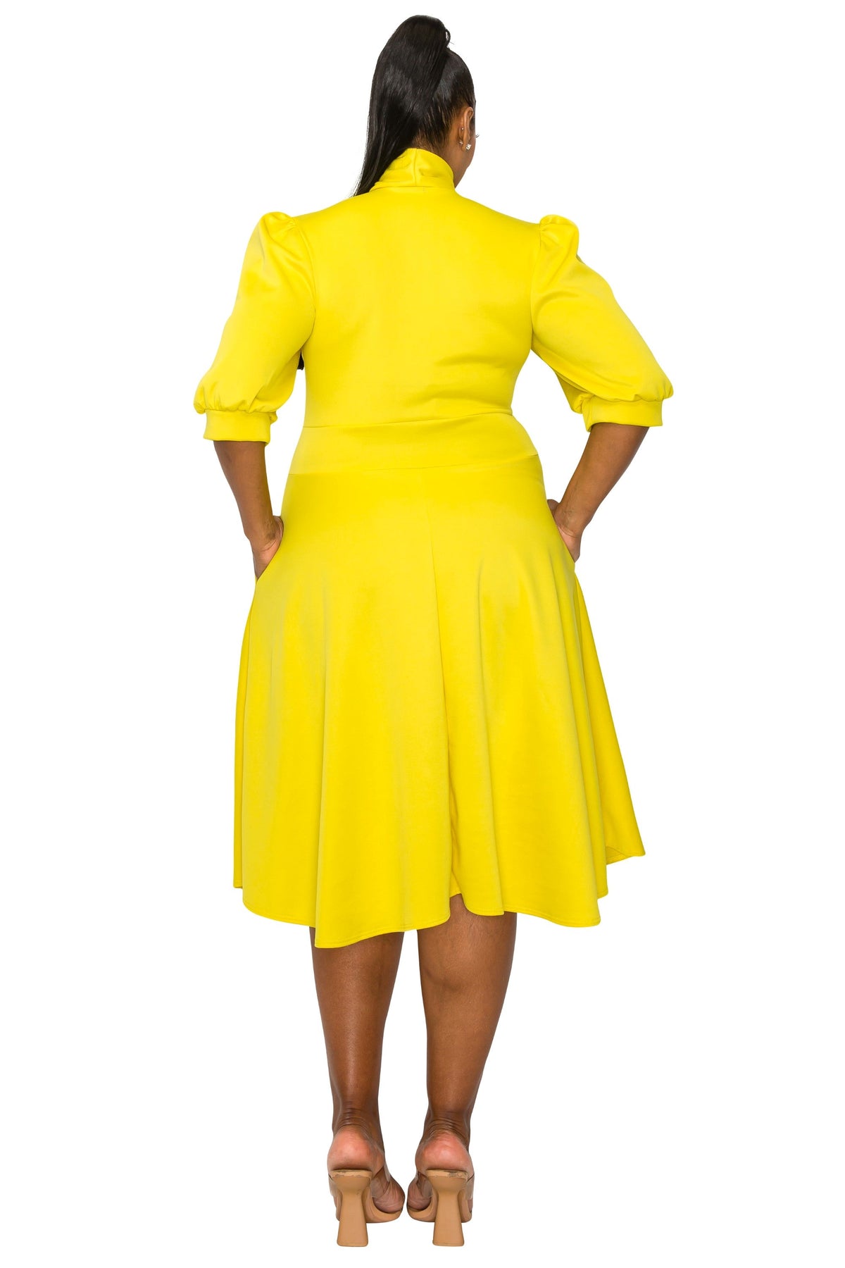 A woman viewed from the back wearing a bright yellow midi dress with puffed elbow-length sleeves, a high mock neck, and a flared skirt, paired with tan block-heel sandals on a white background.