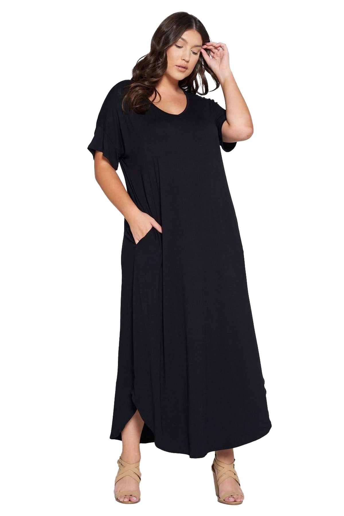 A woman modeling a loose-fitting black maxi dress with short sleeves, a round neckline, and side pockets, paired with beige strappy heels against a plain white background.