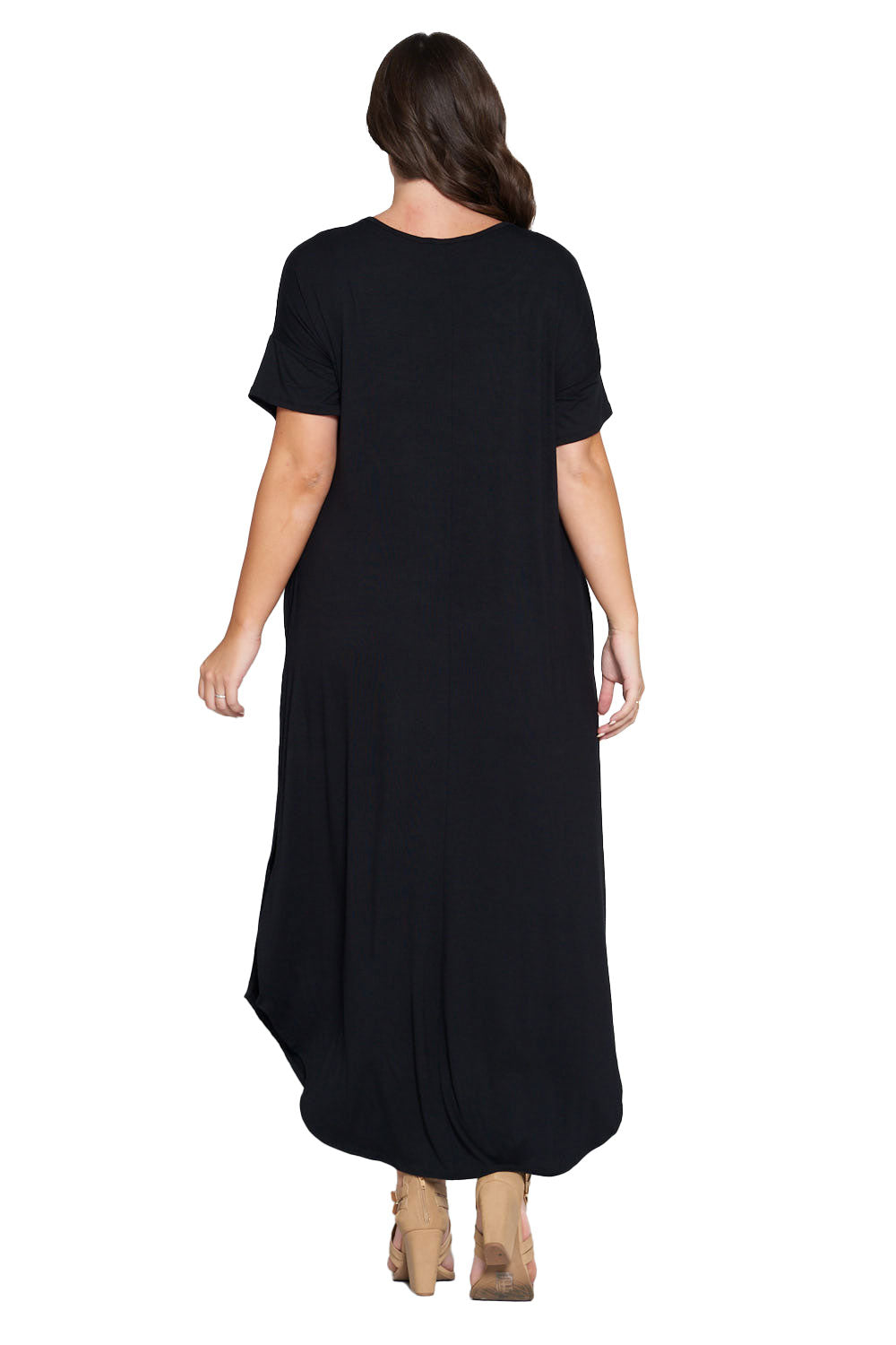 A woman viewed from the back wearing a loose, short-sleeve black maxi dress and tan heeled sandals against a plain white studio background.