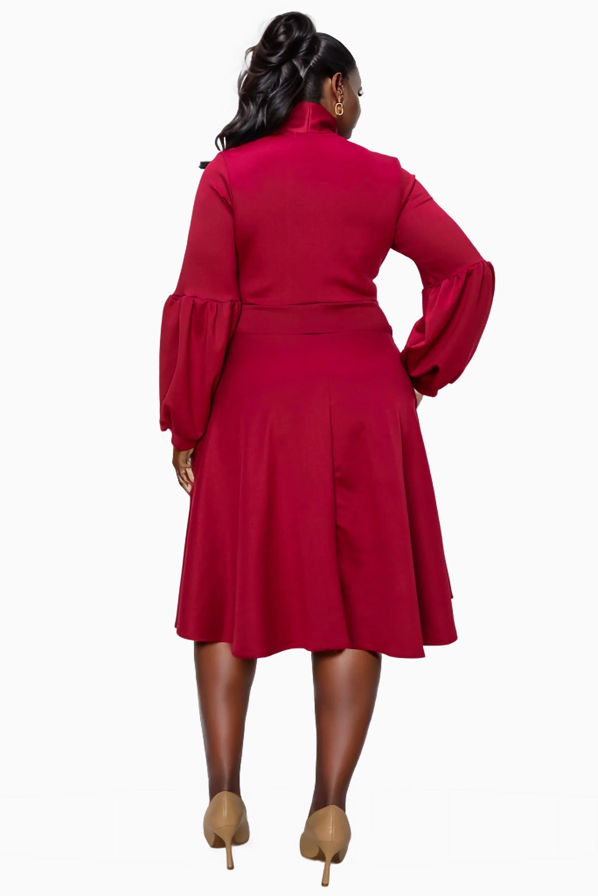 A woman shown from the back wearing a long-sleeve high-neck midi dress in a rich deep red or burgundy, paired with tan high heels, against a plain white background.