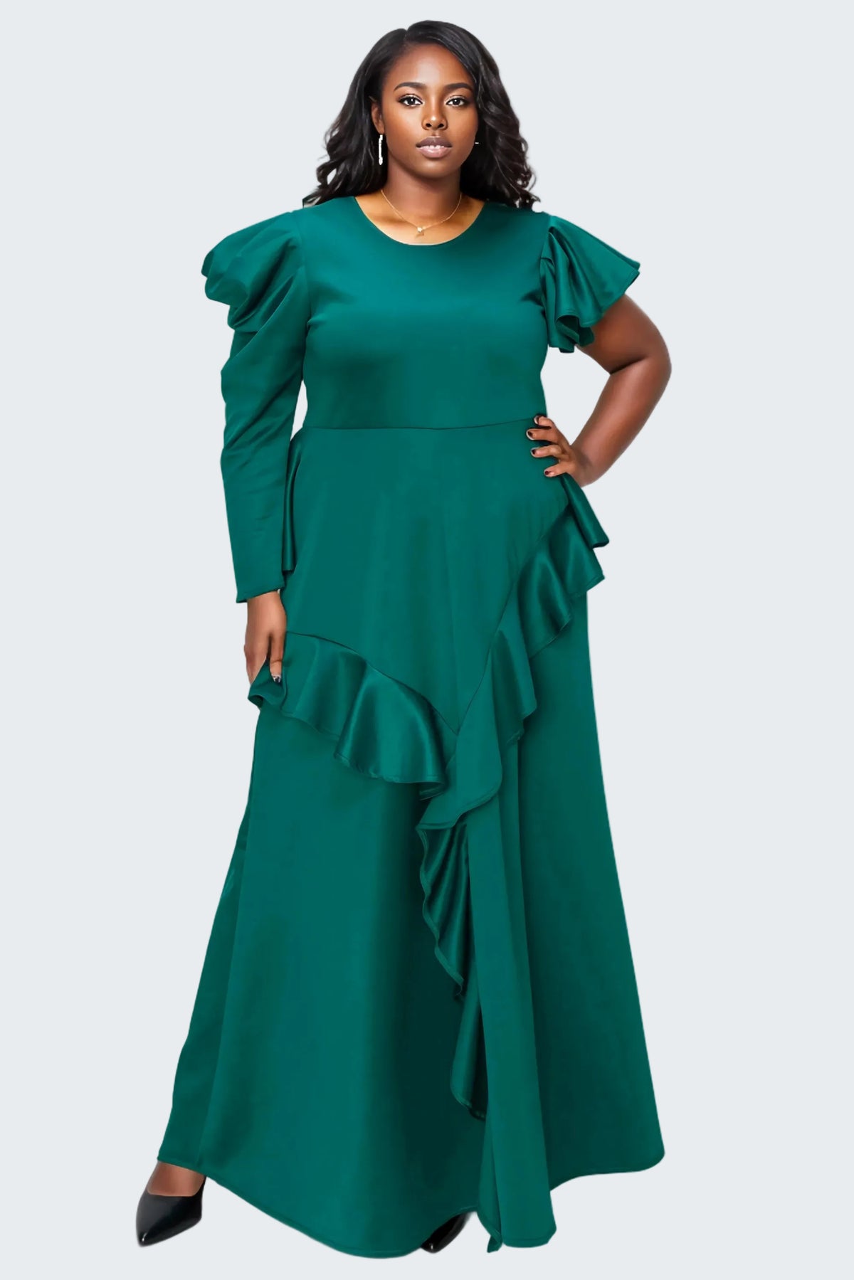 A woman modeling a floor-length emerald green dress with dramatic ruffled sleeves and layered ruffles along the skirt, photographed against a plain white background.