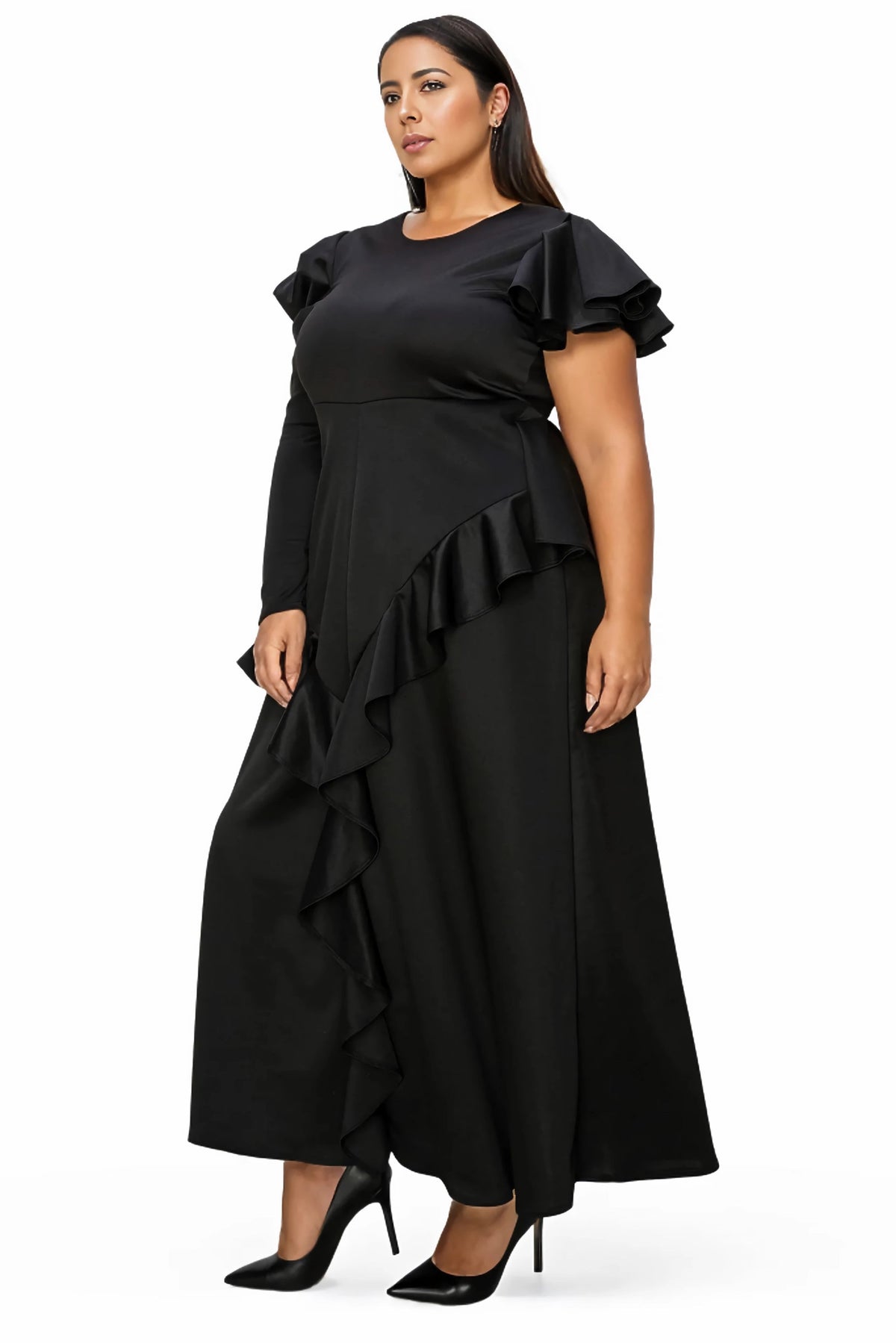 A woman modeling a black long-sleeve maxi dress with ruffled short sleeves and an asymmetrical ruffle hem, paired with black pointed-toe heels, against a plain white background.